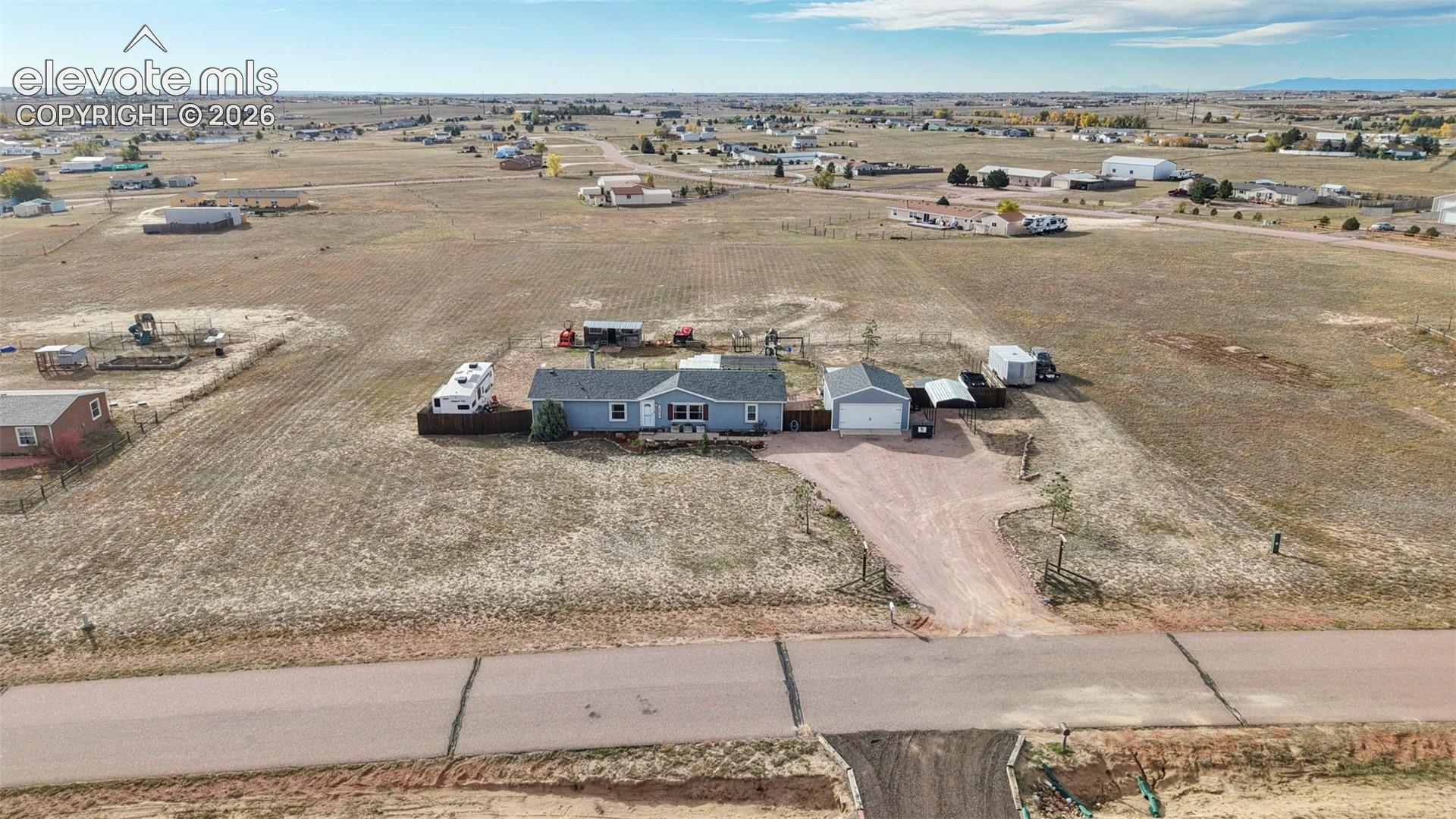 Single-story residence featuring a shingled roof, detached garage, and an expansive acreage lot with a gravel driveway