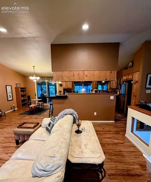 Open-concept living area featuring wood-finish flooring, vaulted ceilings, recessed lighting, and a partial wall with wood paneling separating the kitchen