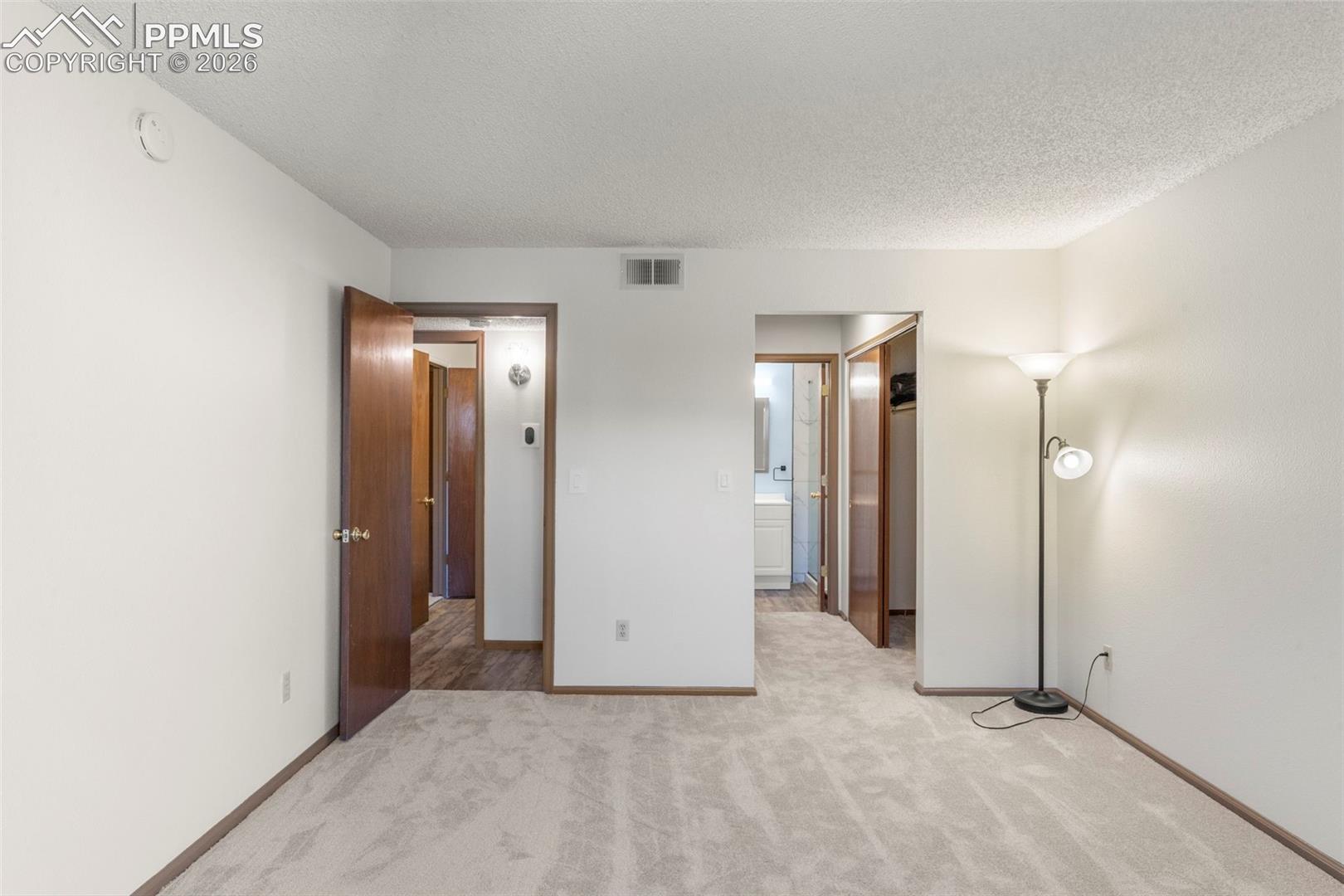 Unfurnished bedroom with light colored carpet, a textured ceiling, and connected bathroom