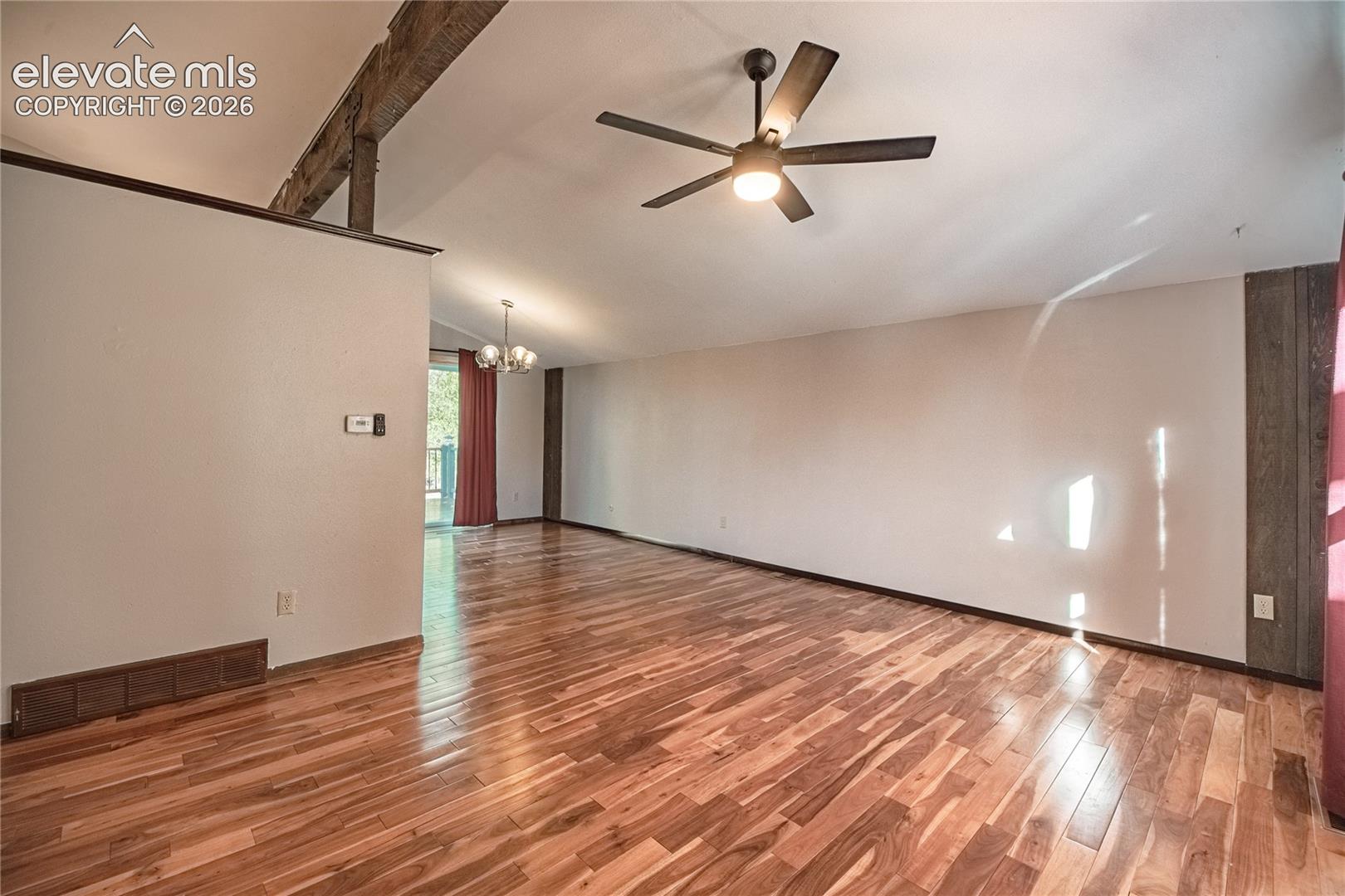 Vaulted ceilings featuring exposed timber beams, wood-finish flooring, and a central ceiling fan