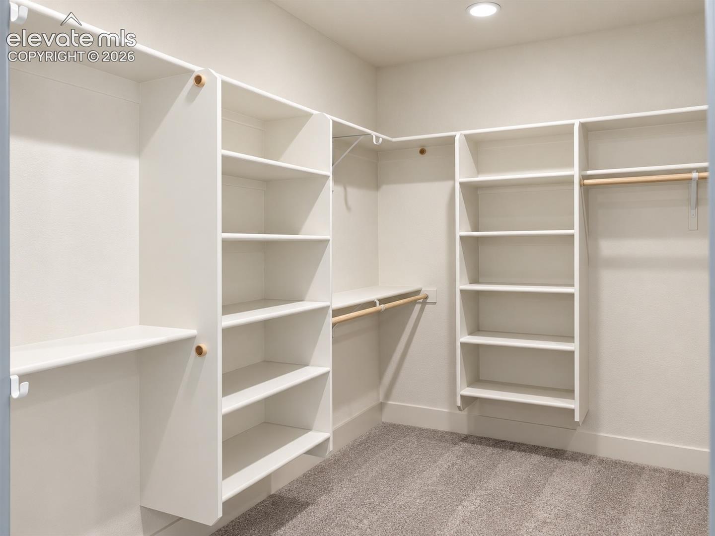 Recessed ceiling lighting, white built-in shelving, natural wood finish hanging rods, and light gray carpet