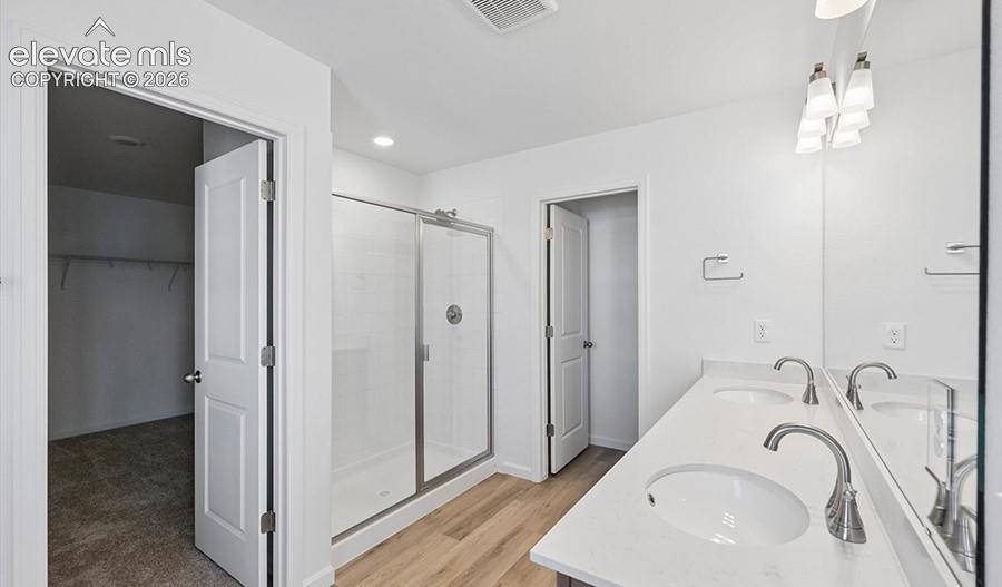 Dual-sink vanity with light-toned countertop, walk-in shower with glass enclosure, and wood-finish flooring