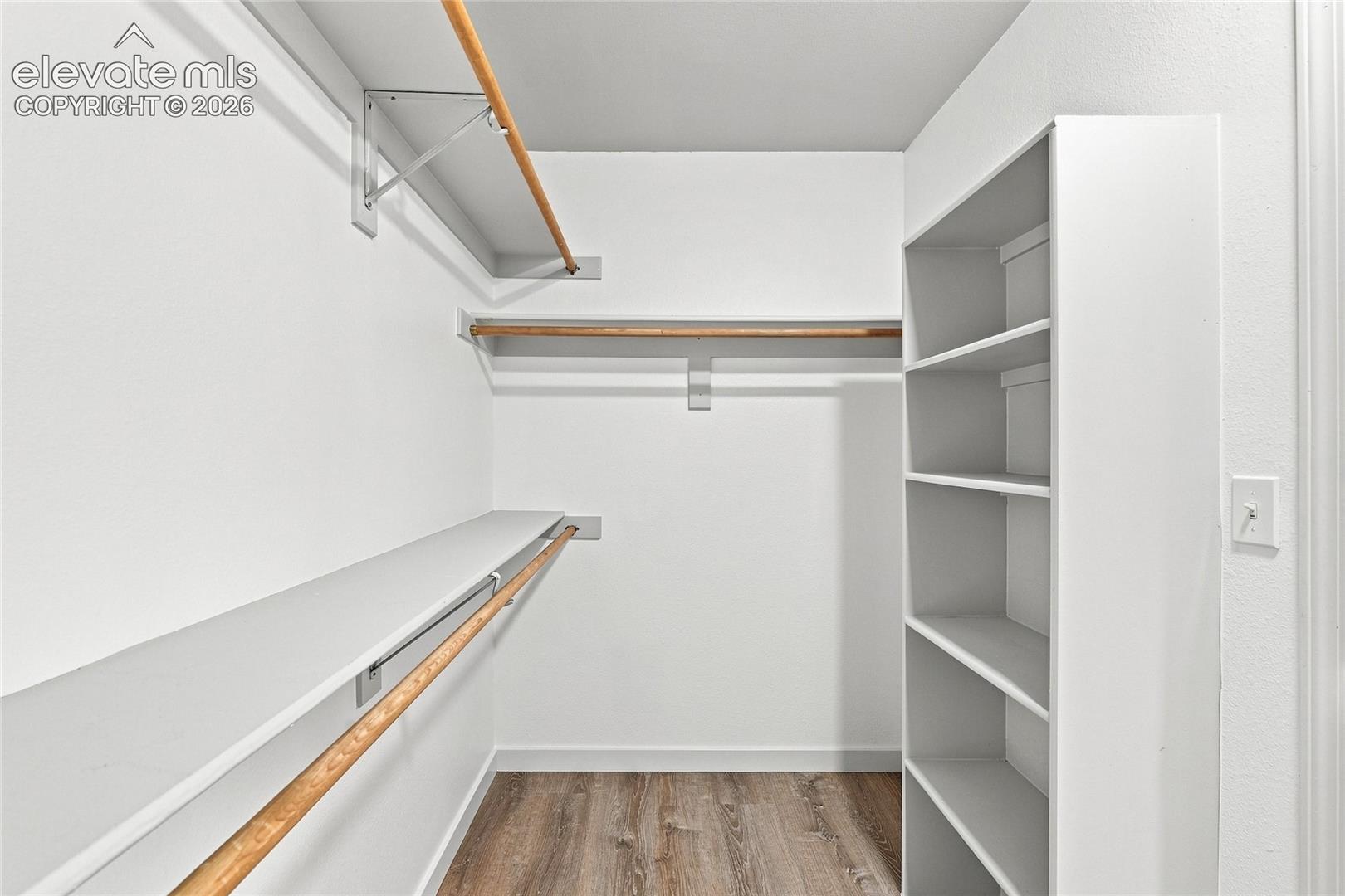 Wood-finish flooring with white baseboards, built-in shelving, white walls, and two clothing rods