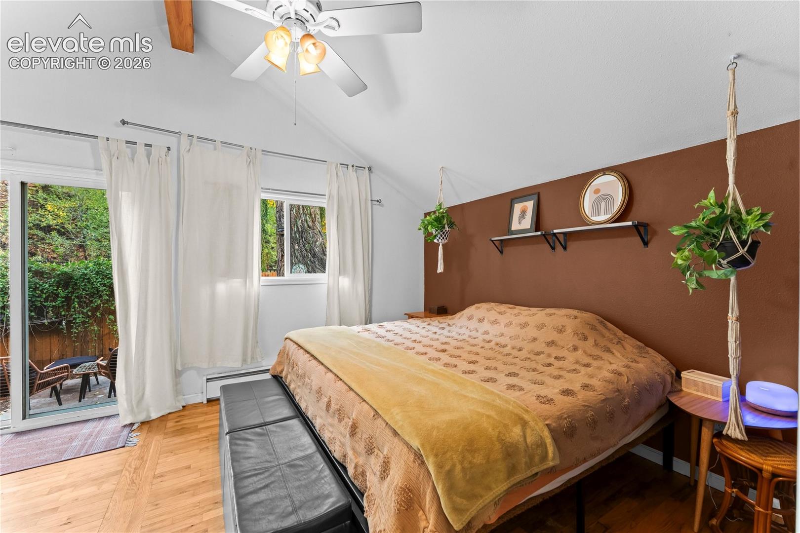 Vaulted ceiling featuring a central ceiling fan and exposed wooden beam, accented by wood-finish flooring and a sliding glass door