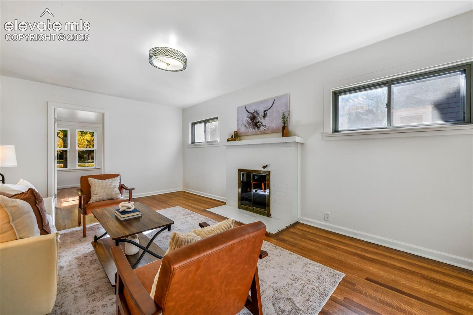 Interior space featuring wood-finish flooring, a painted brick fireplace with a mantel, sliding windows, and a flush-mount circular ceiling fixture