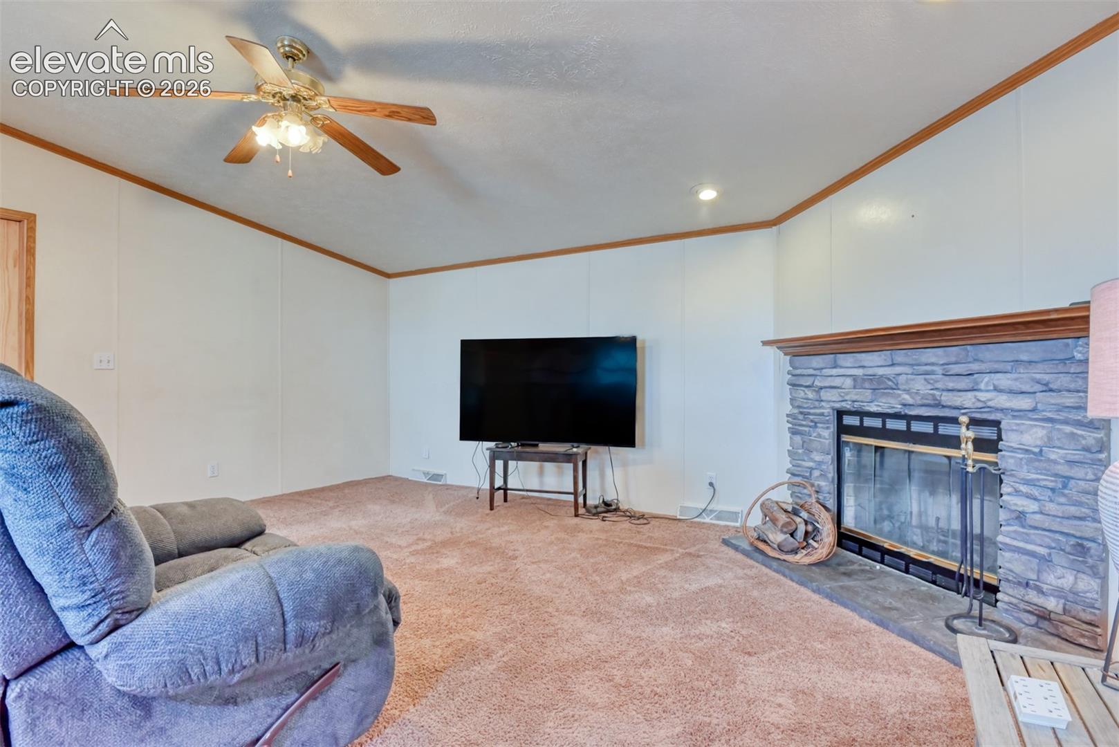 Living space featuring a stone fireplace with a wood mantle, recessed lighting, a ceiling fan, and paneled walls