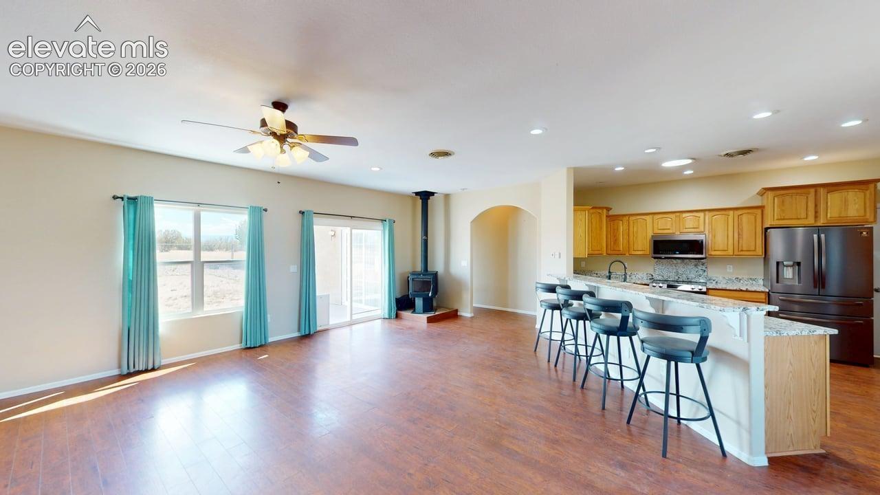 Open-concept living area featuring wood-finish flooring, a ceiling fan, and a built-in wood-burning stove