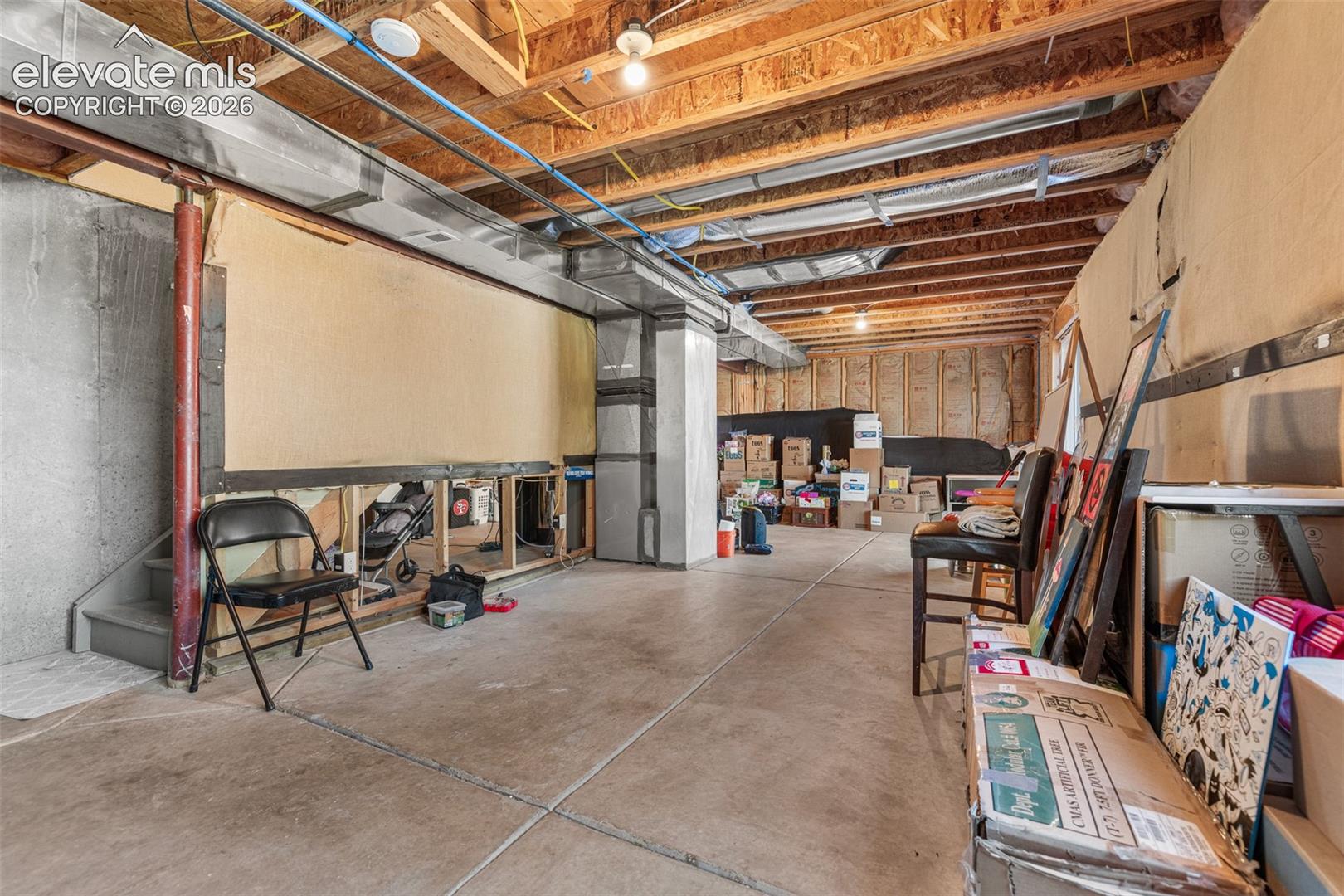 Unfinished lower level featuring concrete flooring, exposed wooden ceiling joists, concrete foundation walls, and metal support columns