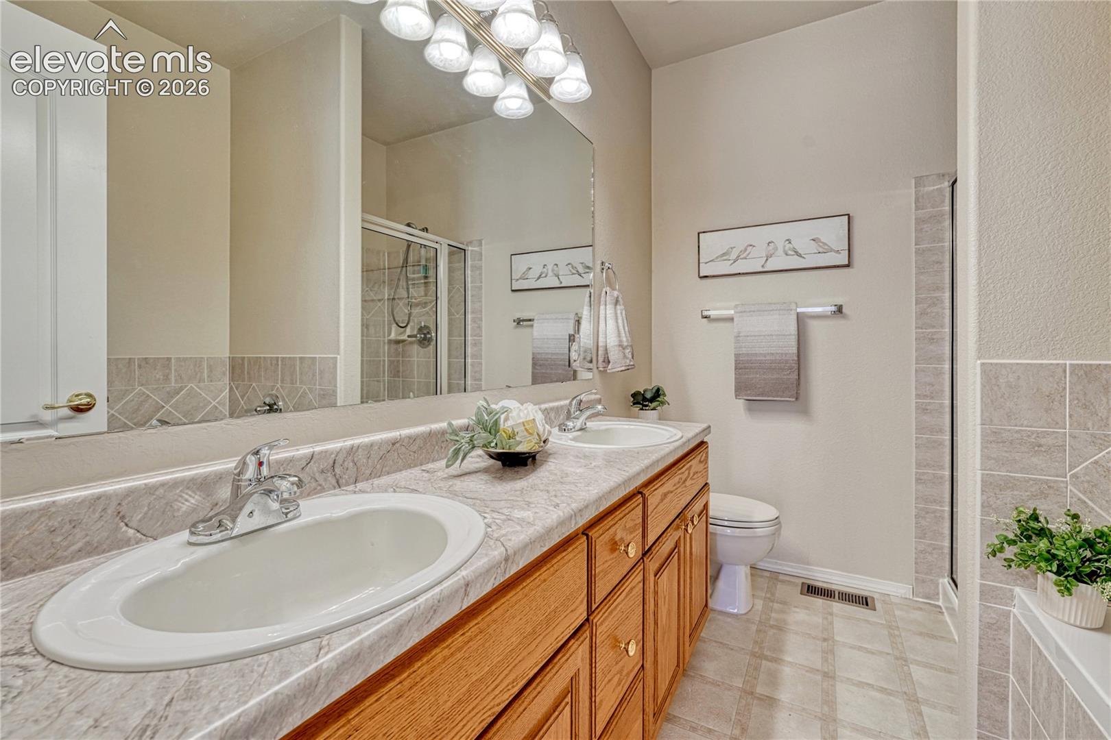 The primary ensuite bath features a double-sink oak vanity, expansive plate-glass mirror, and neutral vinyl flooring
