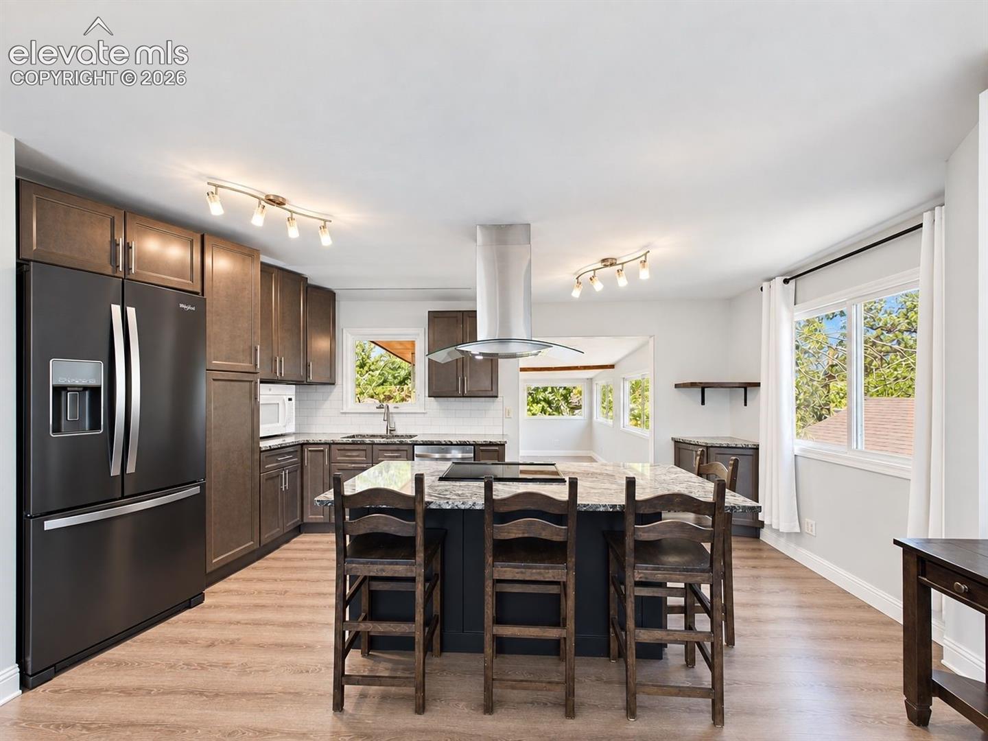 Wide kitchen view showcasing the expansive center island, plentiful storage, stainless steel appliances, and multiple windows bringing natural light into the space.