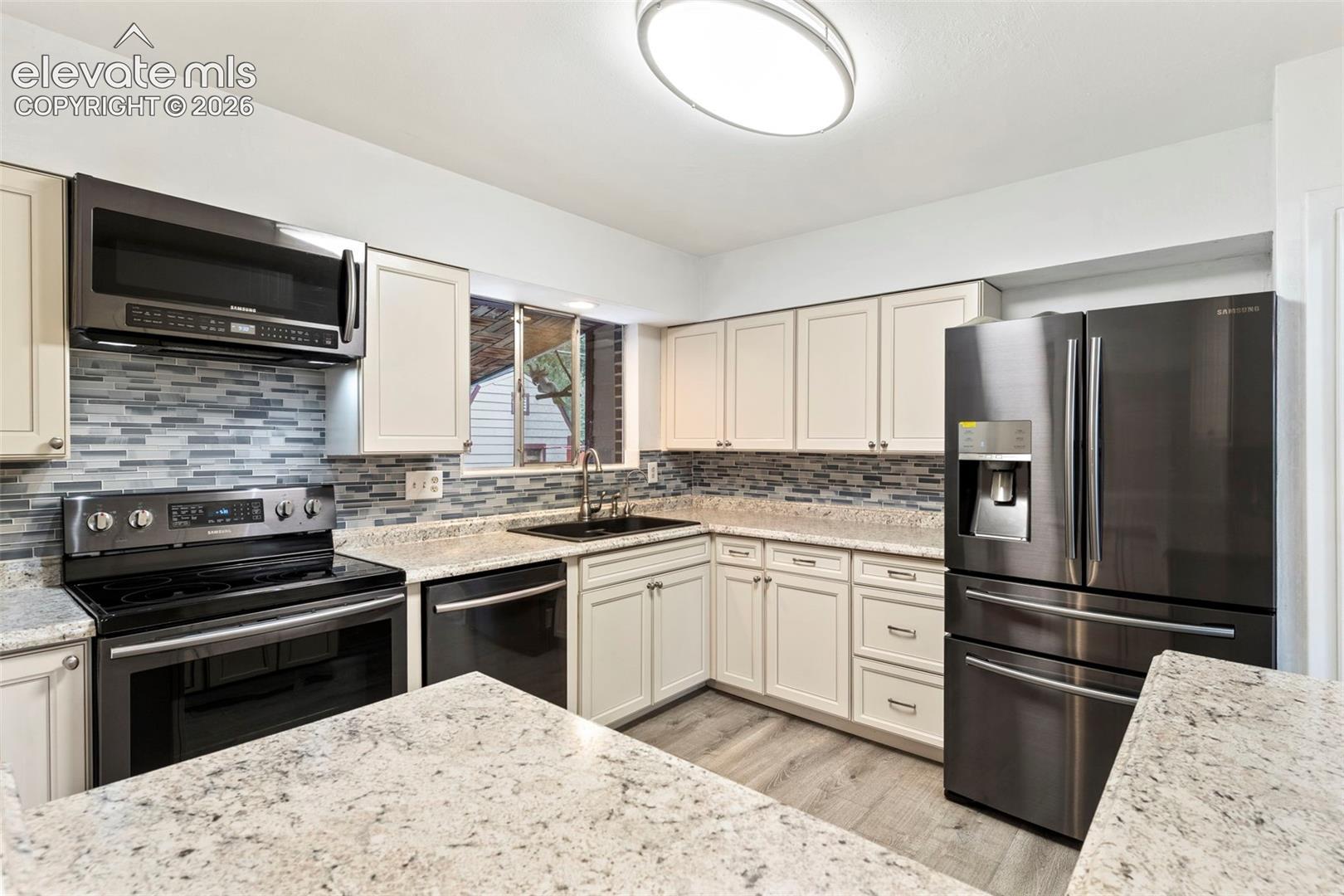 Cream cabinetry, granite countertops, stainless steel appliances, tile backsplash, and wood-finish flooring