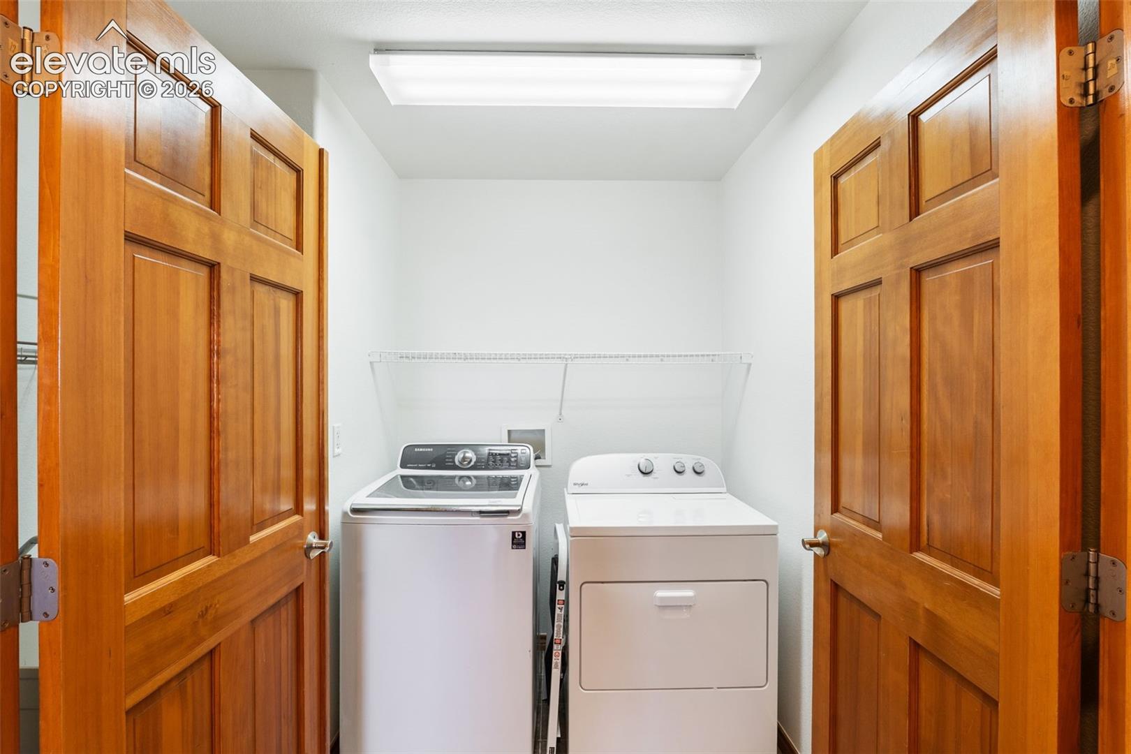 Dedicated laundry space featuring dual six-panel wood doors, overhead flush-mount lighting, and integrated wall-mounted shelving