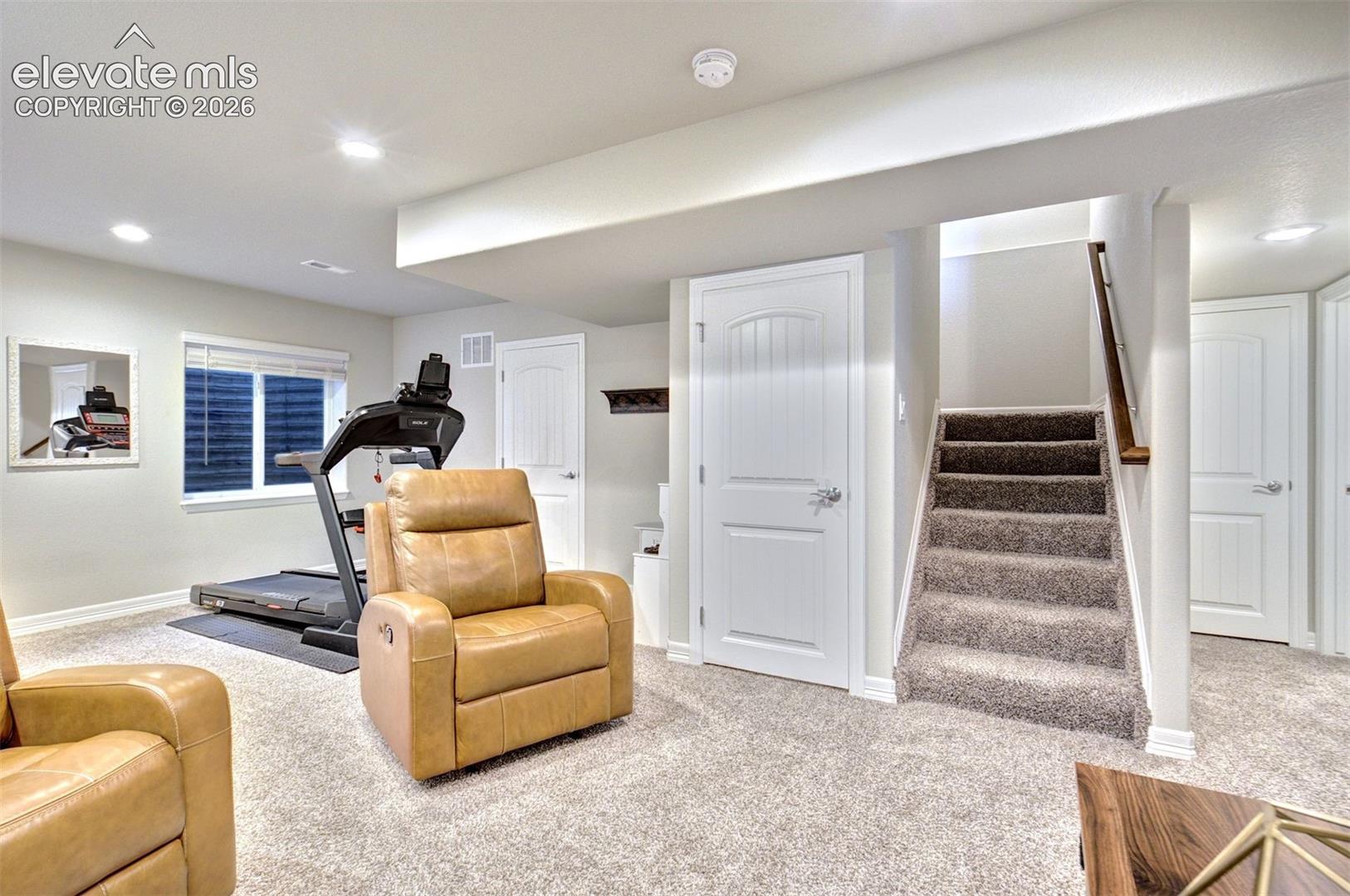 Neutral-toned interior space featuring recessed lighting, wall-to-wall carpeting, three-panel interior doors, and a staircase with a wooden handrail
