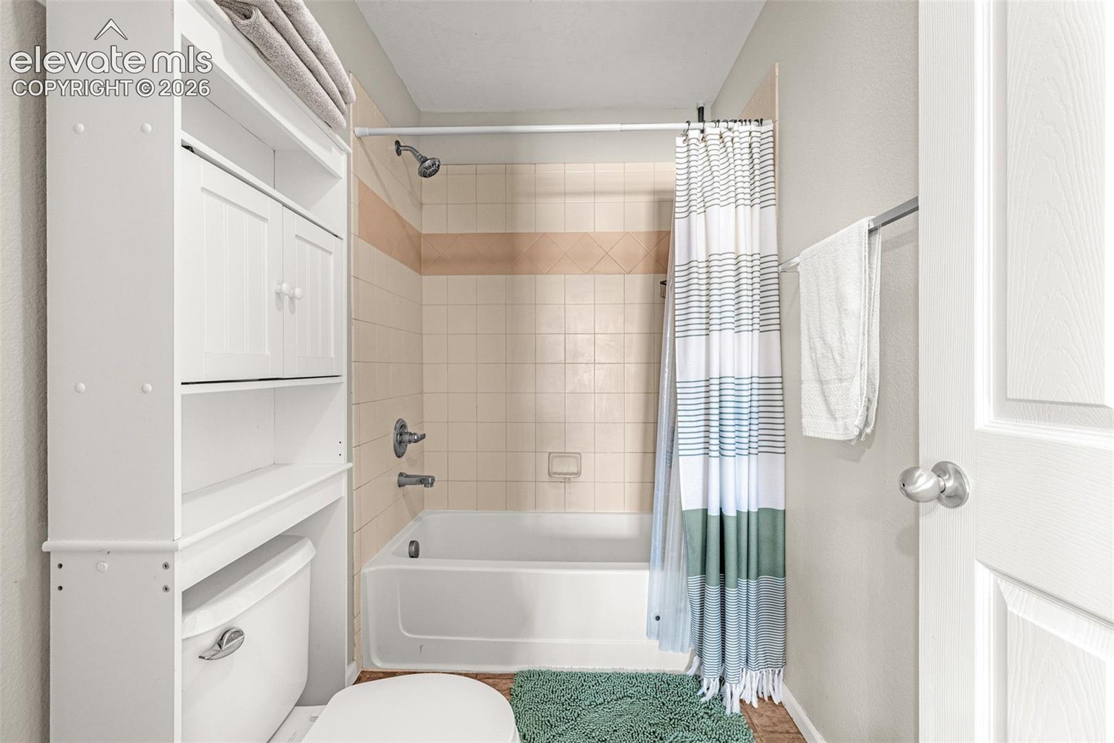 Built-in over-toilet storage cabinetry, white paneled door, and a tiled shower-over-tub combination