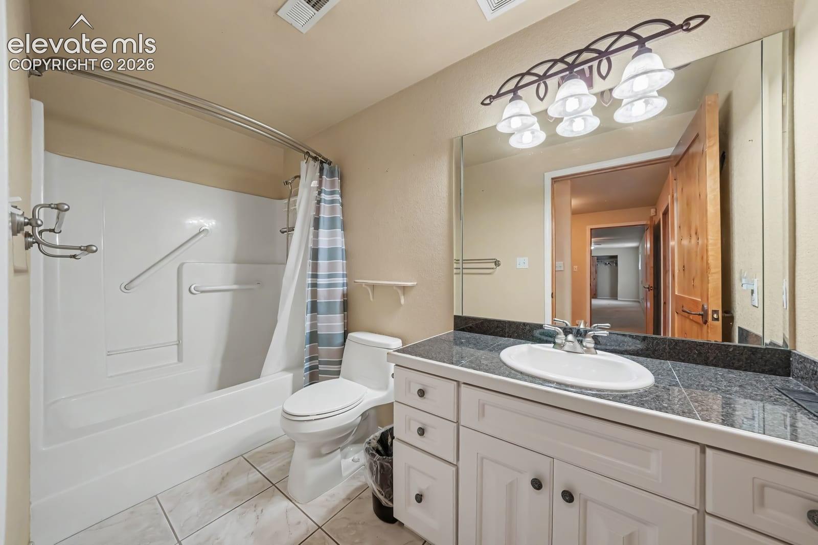 Bathroom featuring white cabinetry, dark stone-finish countertop with an integrated oval sink, full-width wall mirror, and a tub-shower combination with tile-finish flooring