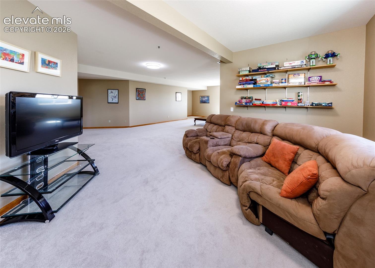 Expansive open-concept room featuring neutral wall tones, wall-to-wall carpeting, and installed wall-mounted shelving
