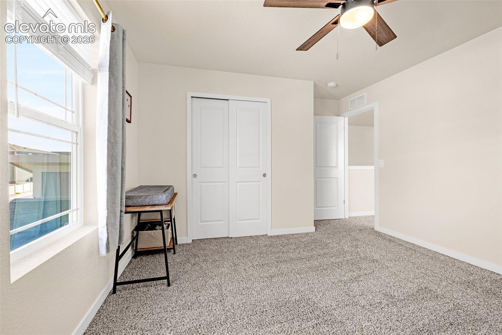 Plush carpeting, neutral wall colors, dual-pane window, white bi-fold closet doors, and a ceiling fan with integrated lighting