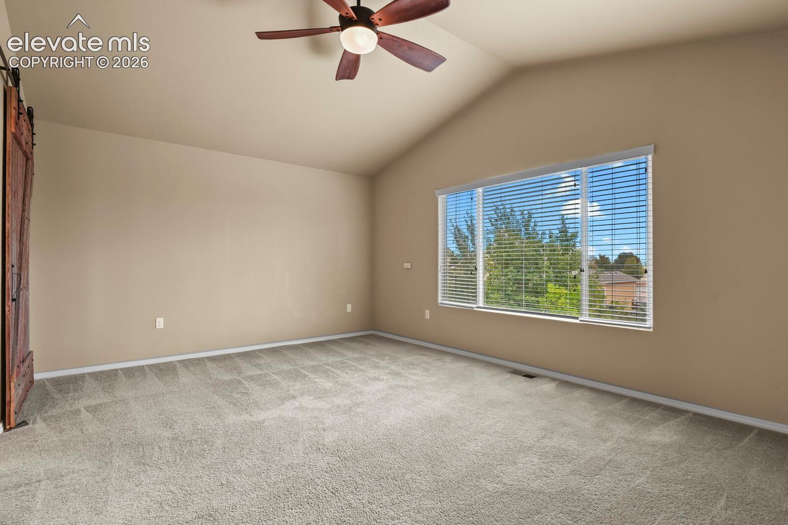 Vaulted ceiling with a ceiling fan, large window with blinds, and light-toned carpeting