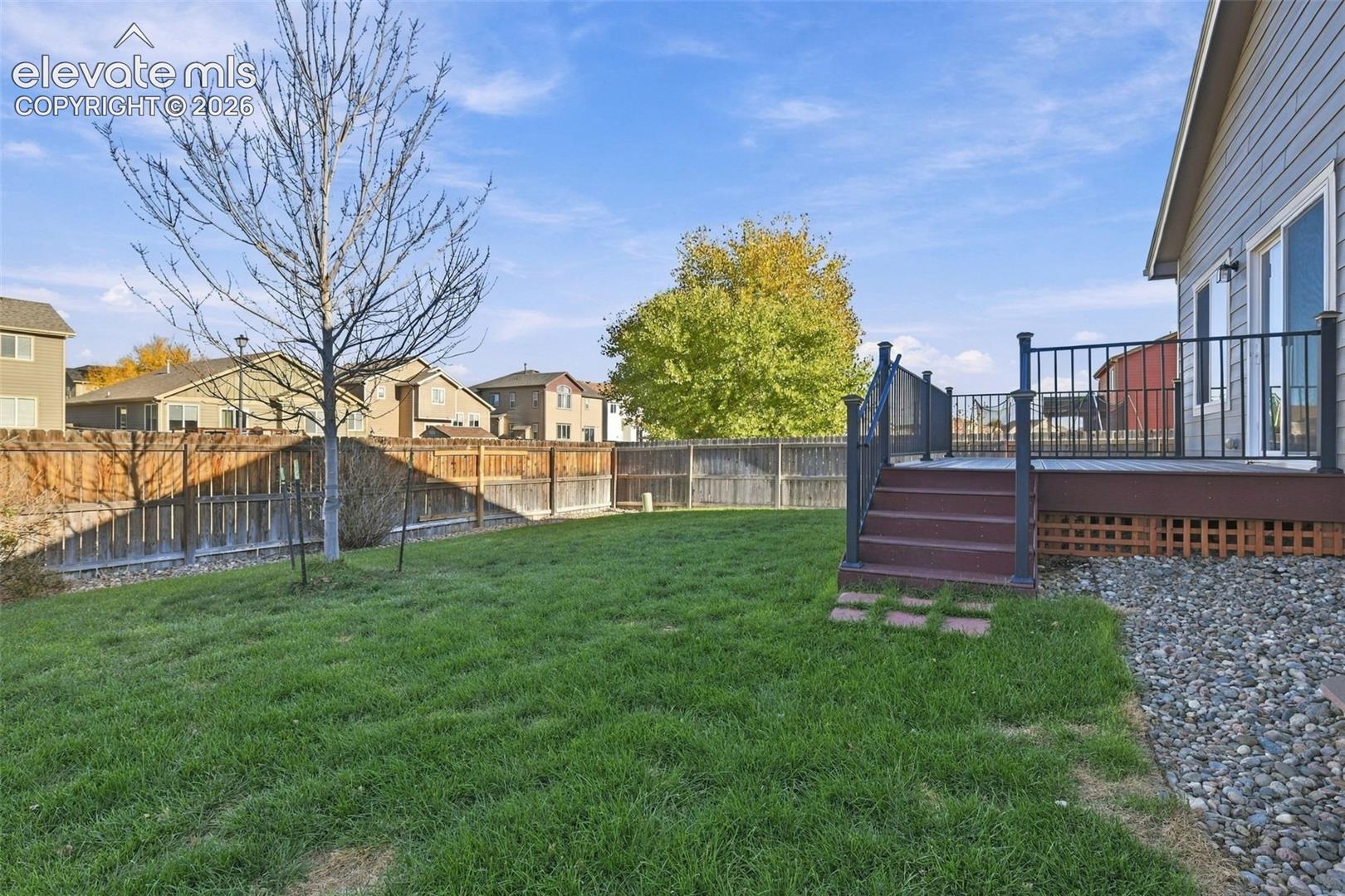 Backyard featuring a raised composite deck, black metal railings, a manicured lawn, and perimeter wood fencing
