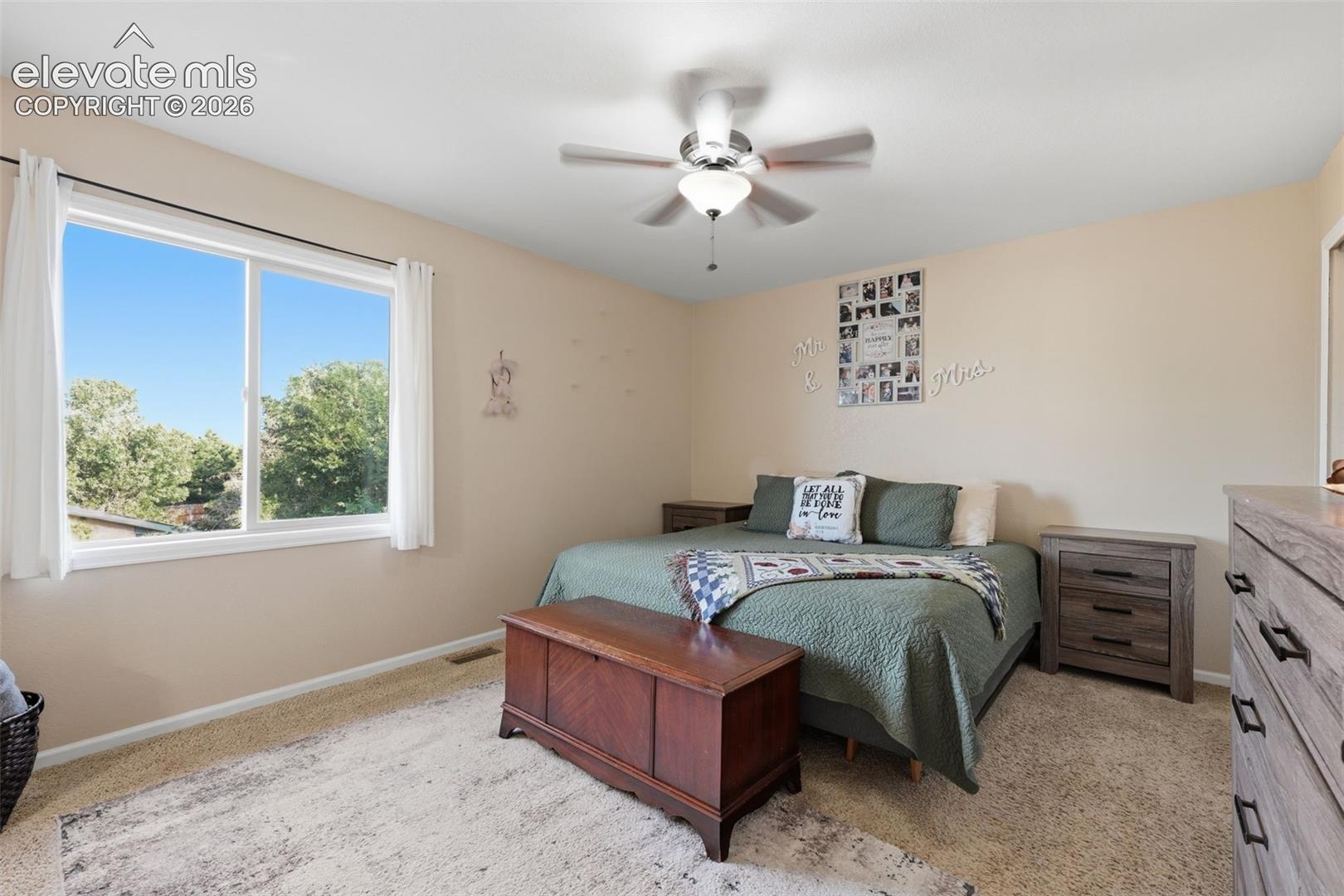 Spacious room featuring a white-framed window, neutral painted walls, textured carpet flooring, and a ceiling fan with integrated lighting