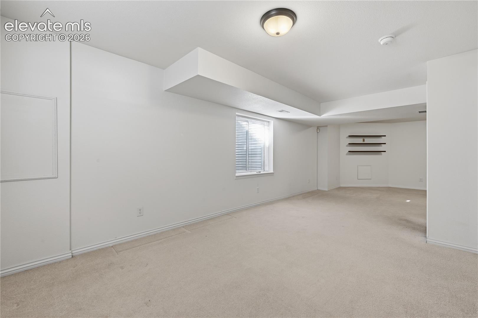 Interior space featuring neutral wall-to-wall carpeting, recessed window with a window well, built-in wall shelving, and a flush-mount ceiling light fixture