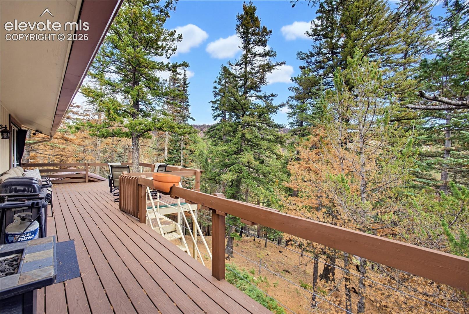 Expansive wooden deck featuring horizontal rail fencing, integrated stairs, and surrounding mature pine trees