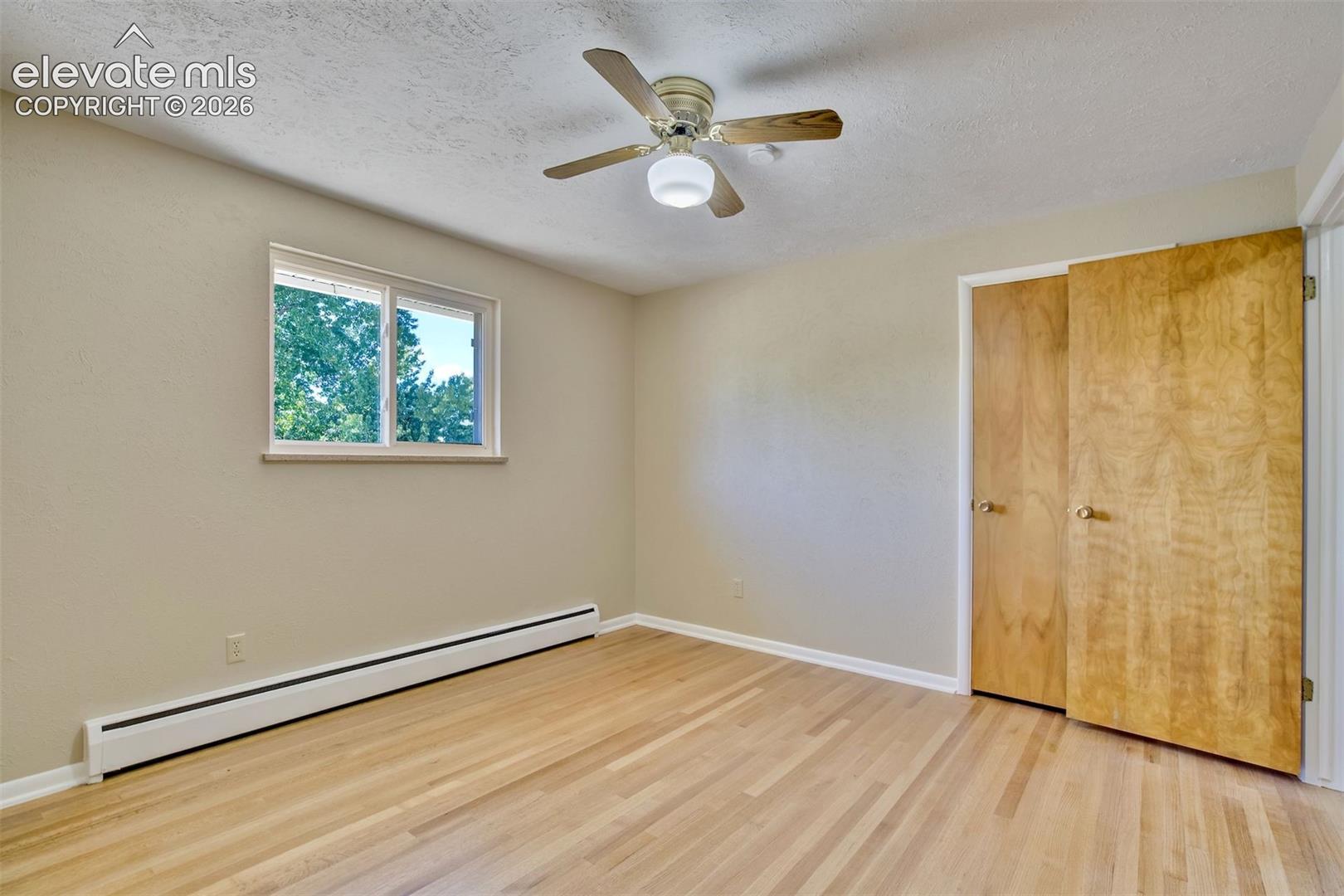 Room featuring wood-finish flooring, a ceiling fan with integrated lighting, a sliding door closet with wood-grain finish, and a window