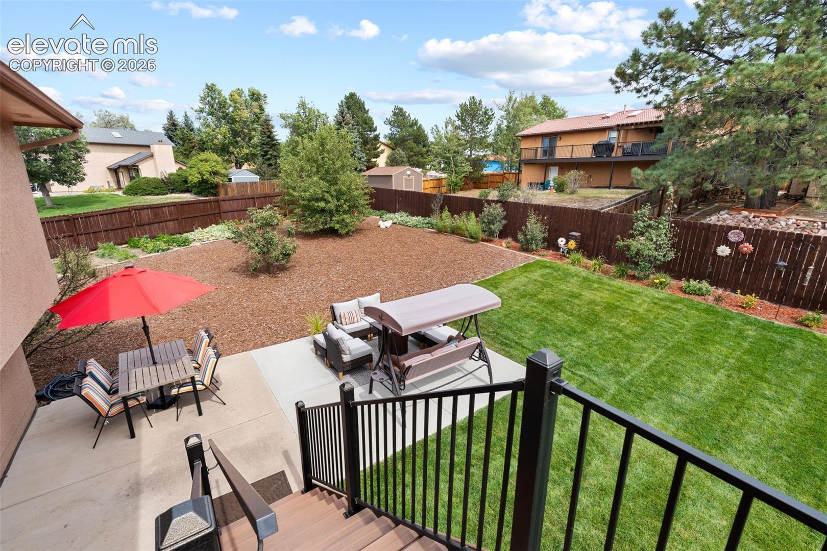 Rear yard featuring a concrete patio, wood-composite stairs with metal railings, mulched garden beds, and perimeter wood fencing