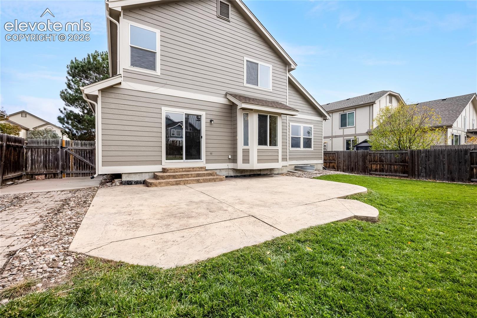 Rear exterior featuring horizontal lap siding, concrete patio, sliding glass door, bay window, and wood perimeter fencing