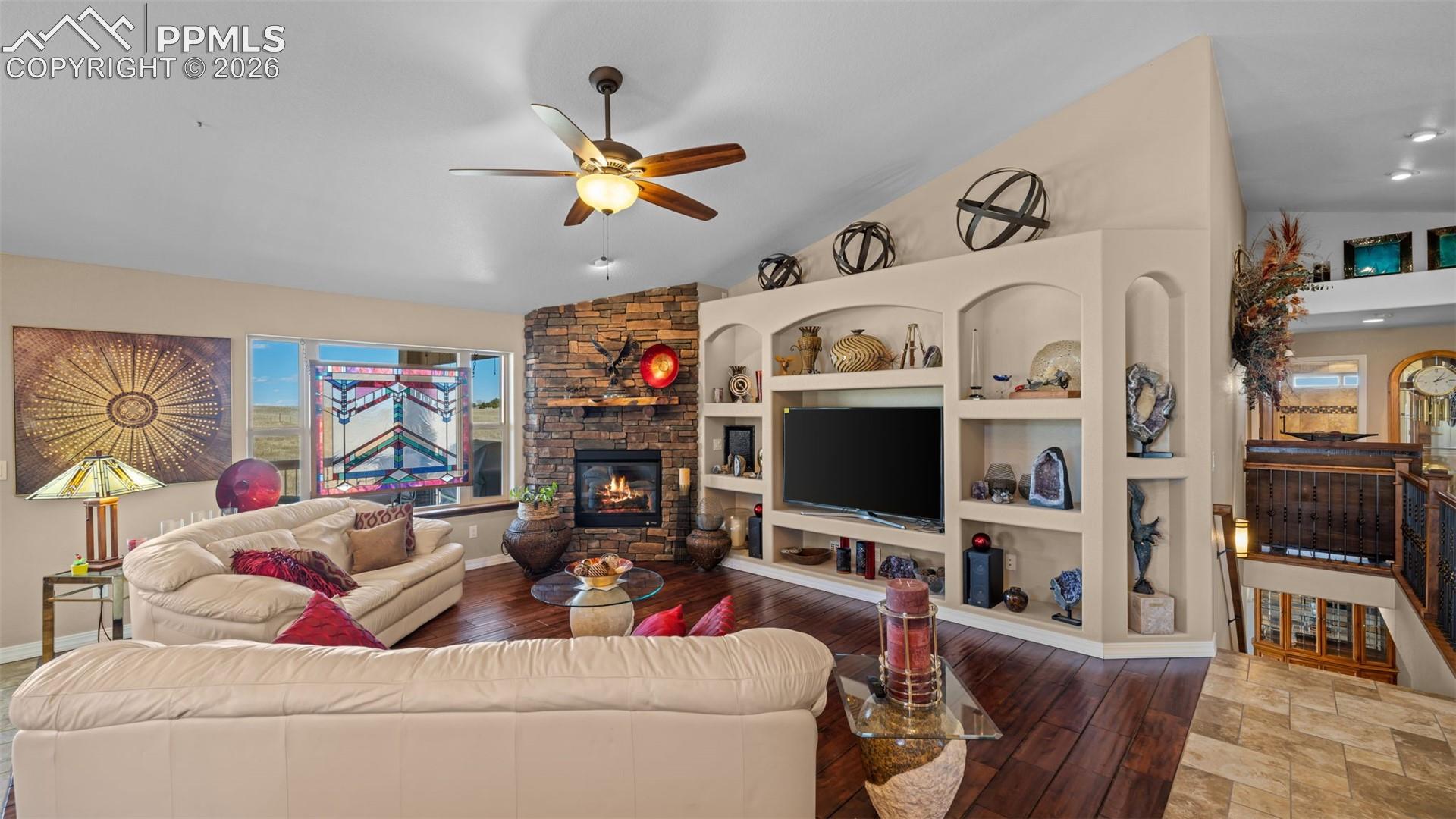 Living area featuring a fireplace, a ceiling fan, hardwood / wood-style flooring, vaulted ceiling, and built in features