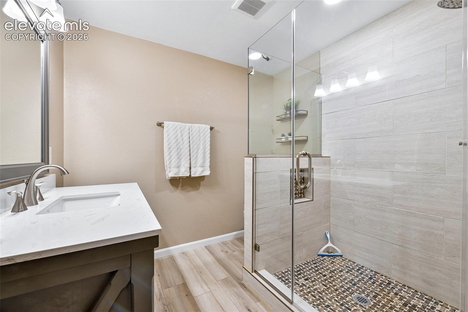 Basement bathroom, Walk-in shower with clear glass enclosure, pebble tile floor, and light tile surround