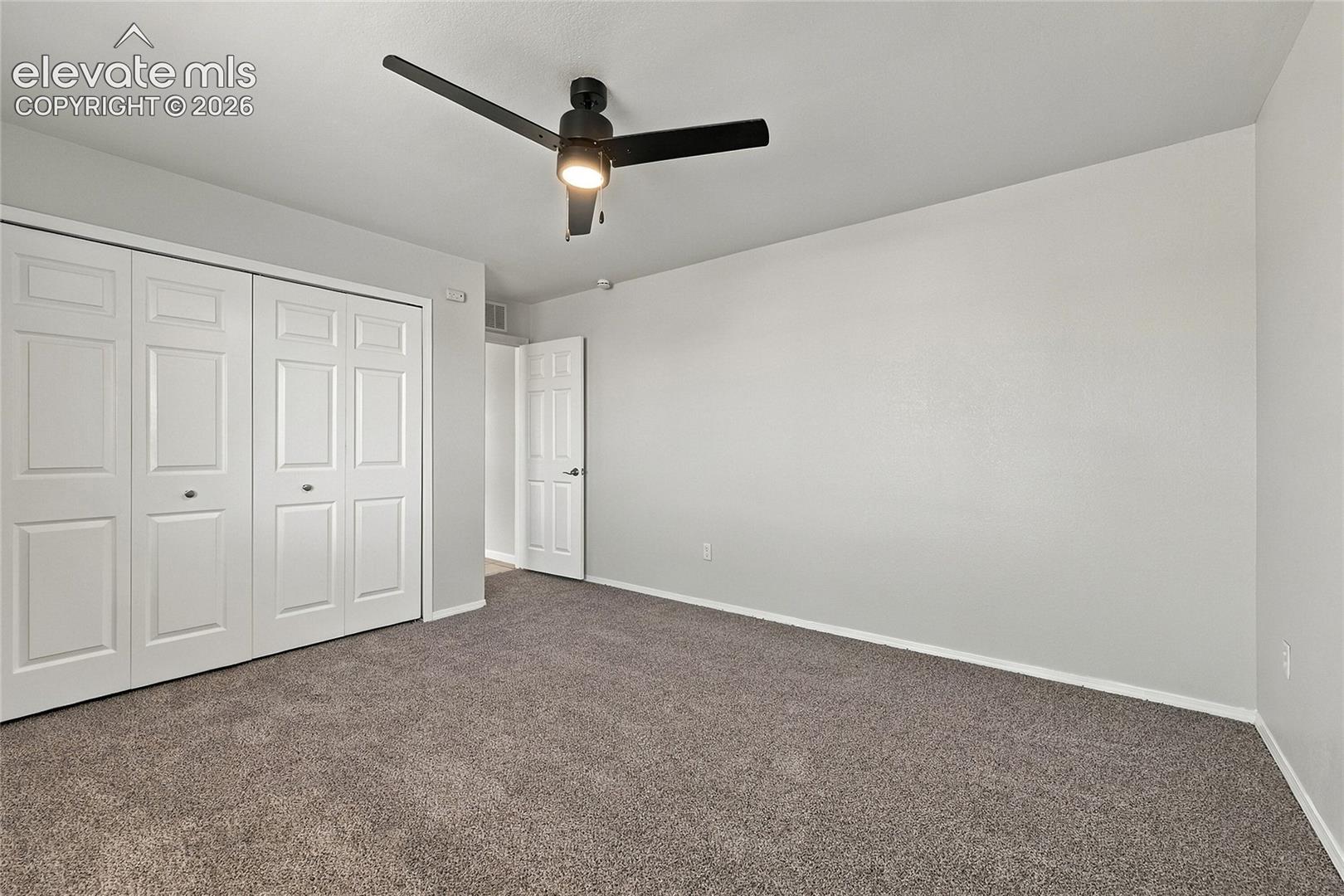 Neutral wall paint, plush carpeting, three-panel closet doors, and a matte black ceiling fan with an integrated light fixture