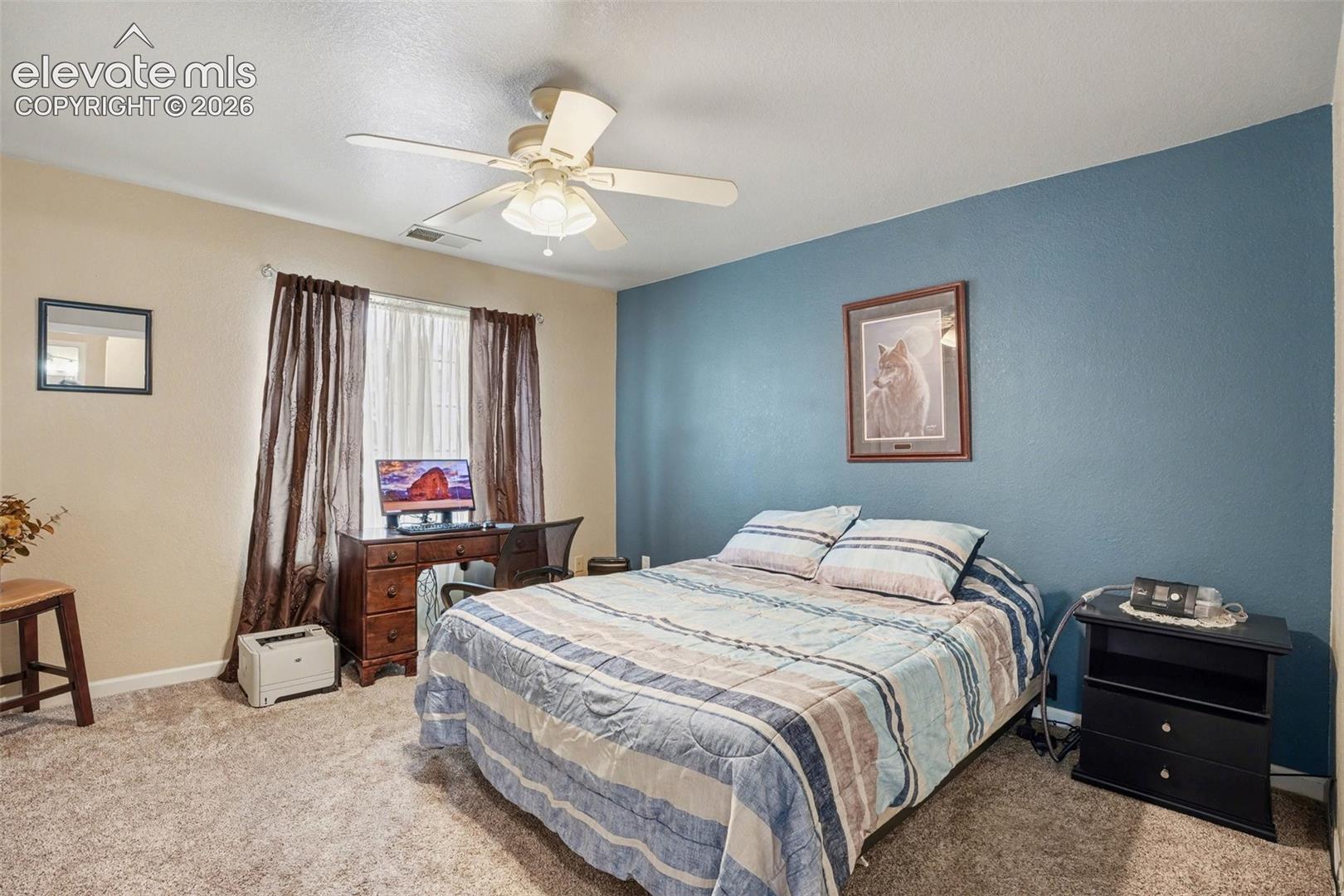 Bedroom featuring wall-to-wall carpeting, a dual-tone paint scheme with a blue accent wall, a central ceiling fan with integrated lighting, and a large window