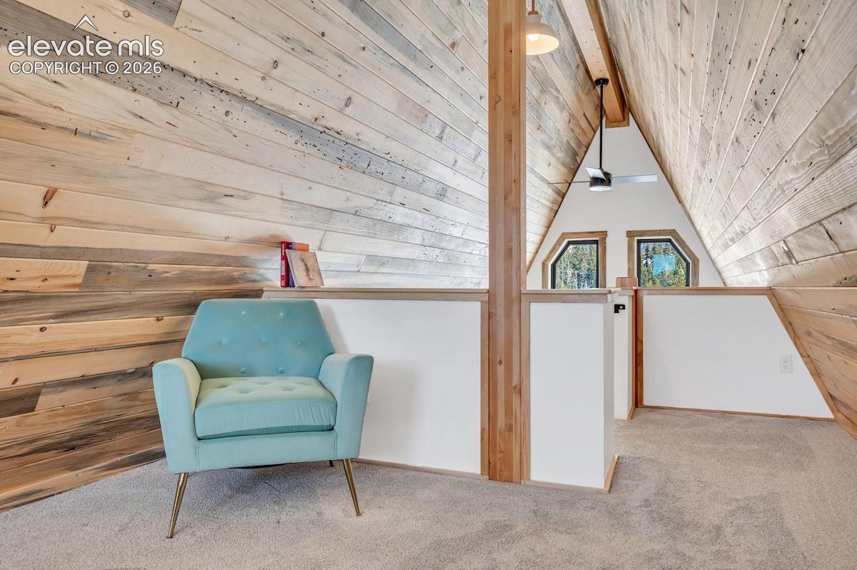 A-frame interior featuring vaulted ceilings with wood-plank paneling, exposed structural timber, carpeted flooring, and multi-faceted windows