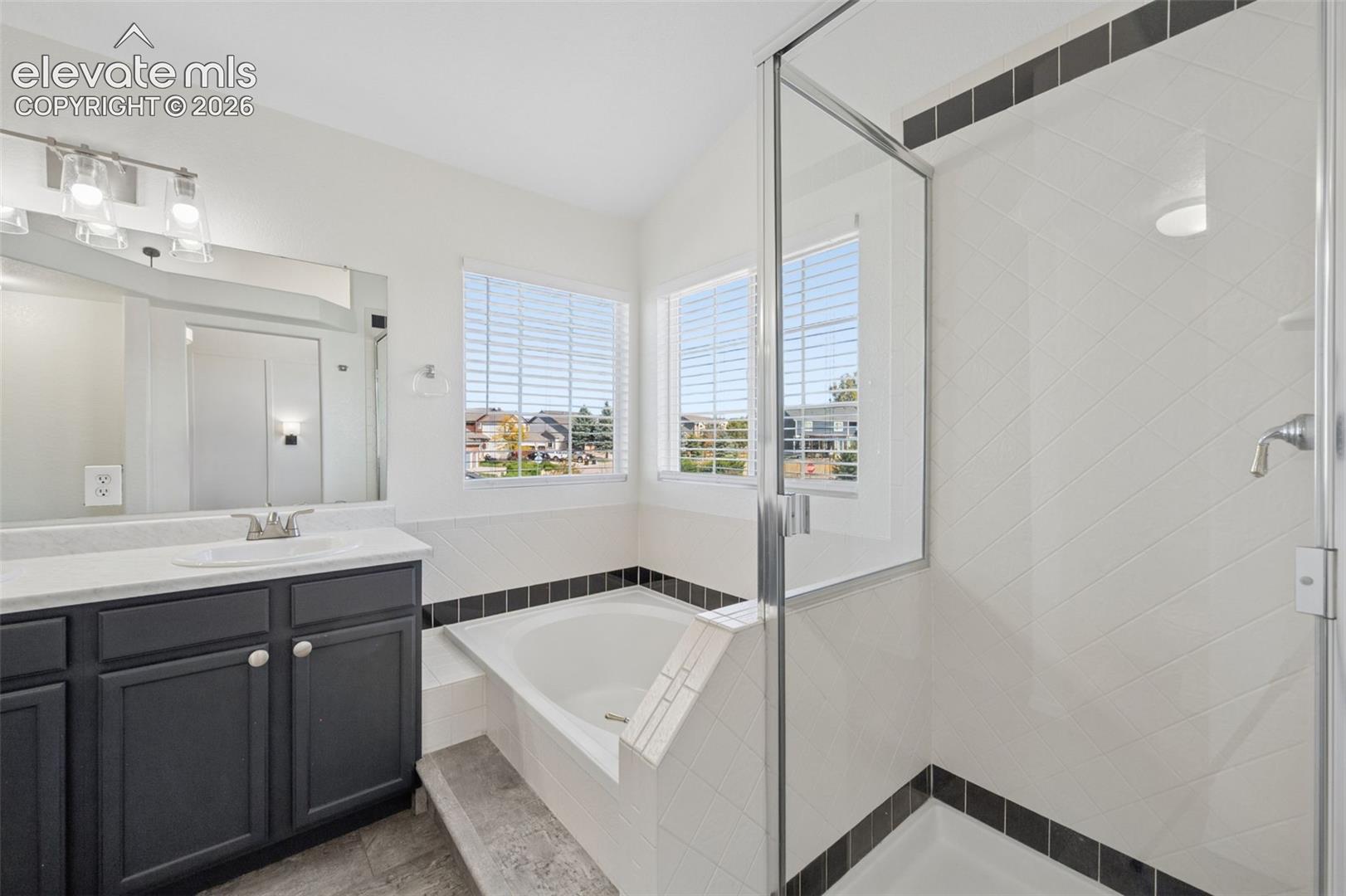 Bathroom featuring a dark-toned vanity with a light countertop, a soaking tub, and a glass-enclosed shower with tiled walls and dark accent detailing