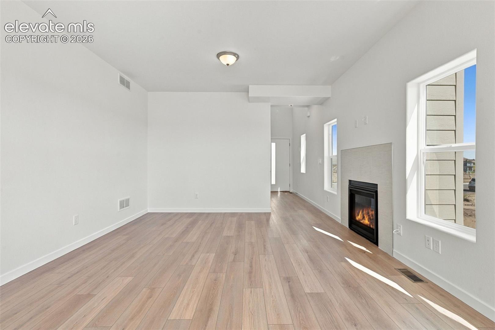 Spacious room featuring wood-finish flooring, multiple windows, a modern fireplace with a tiled surround, and a ceiling-mounted light fixture