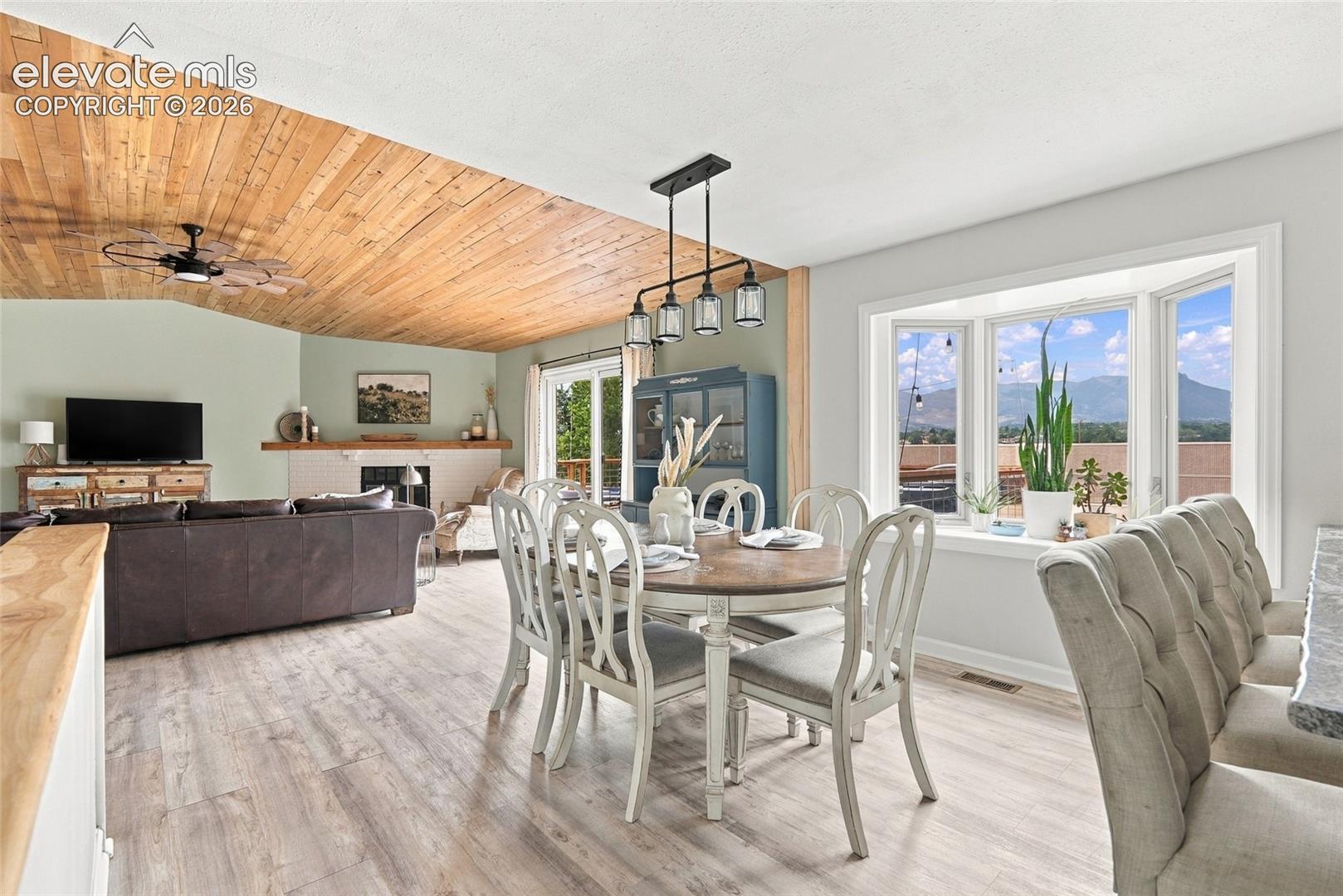 Open-concept living space featuring wood-finish flooring, a wood plank vaulted ceiling, a bay window, and a white tile fireplace