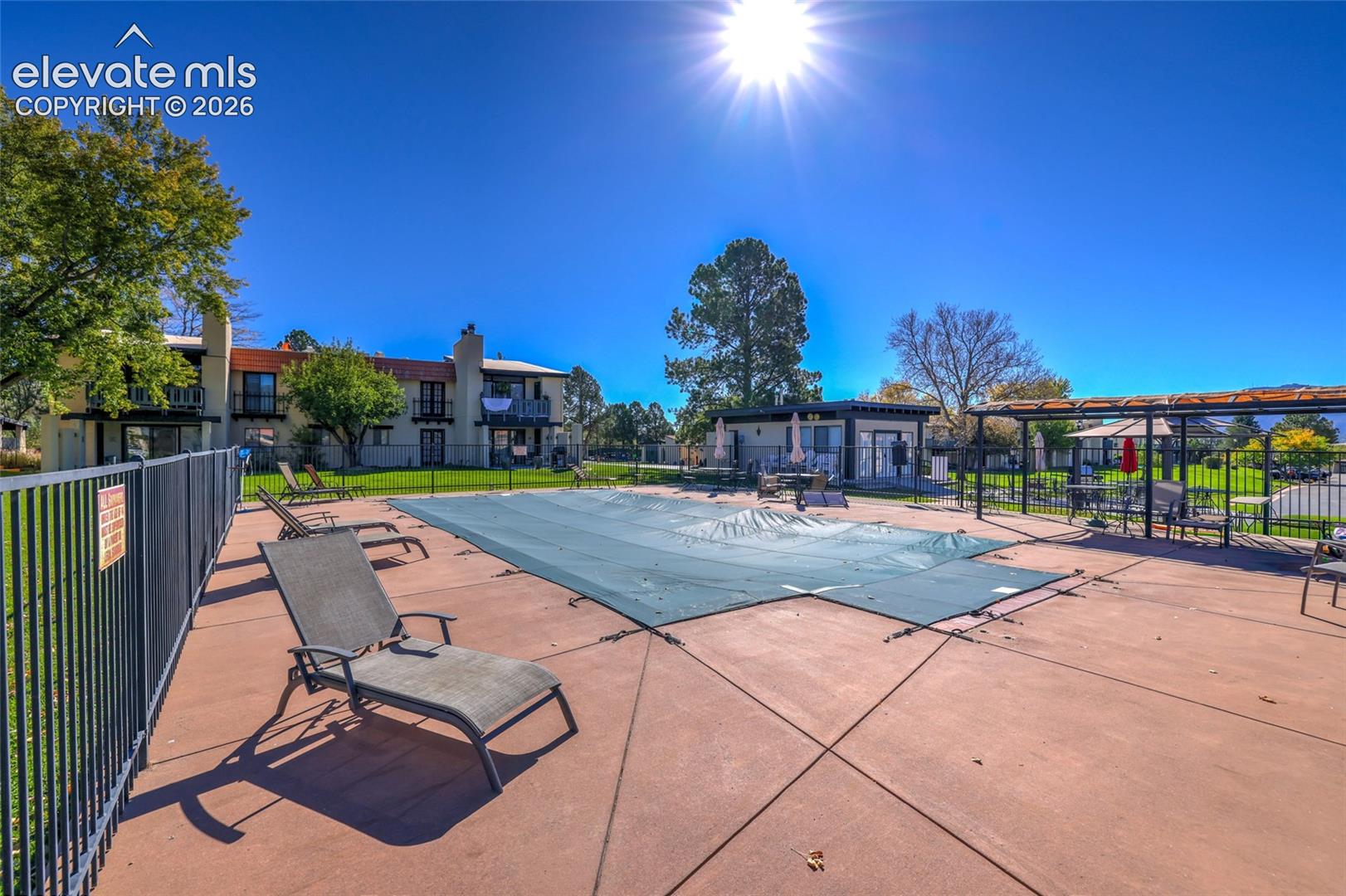 Swimming pool with security fencing, concrete decking, and attached pergola structure
