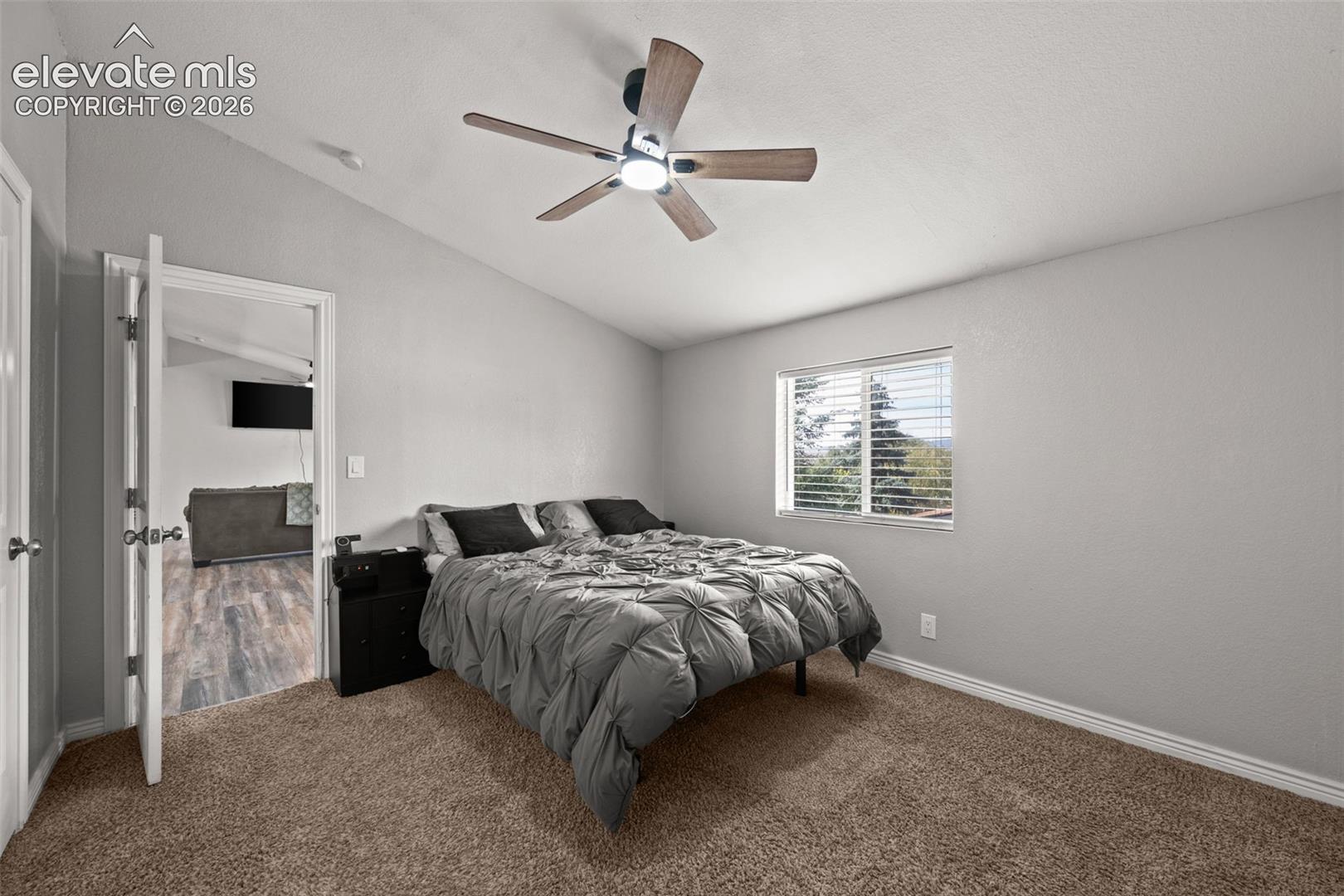 Room featuring neutral-toned carpeting, vaulted ceilings, and a central ceiling fan with integrated lighting