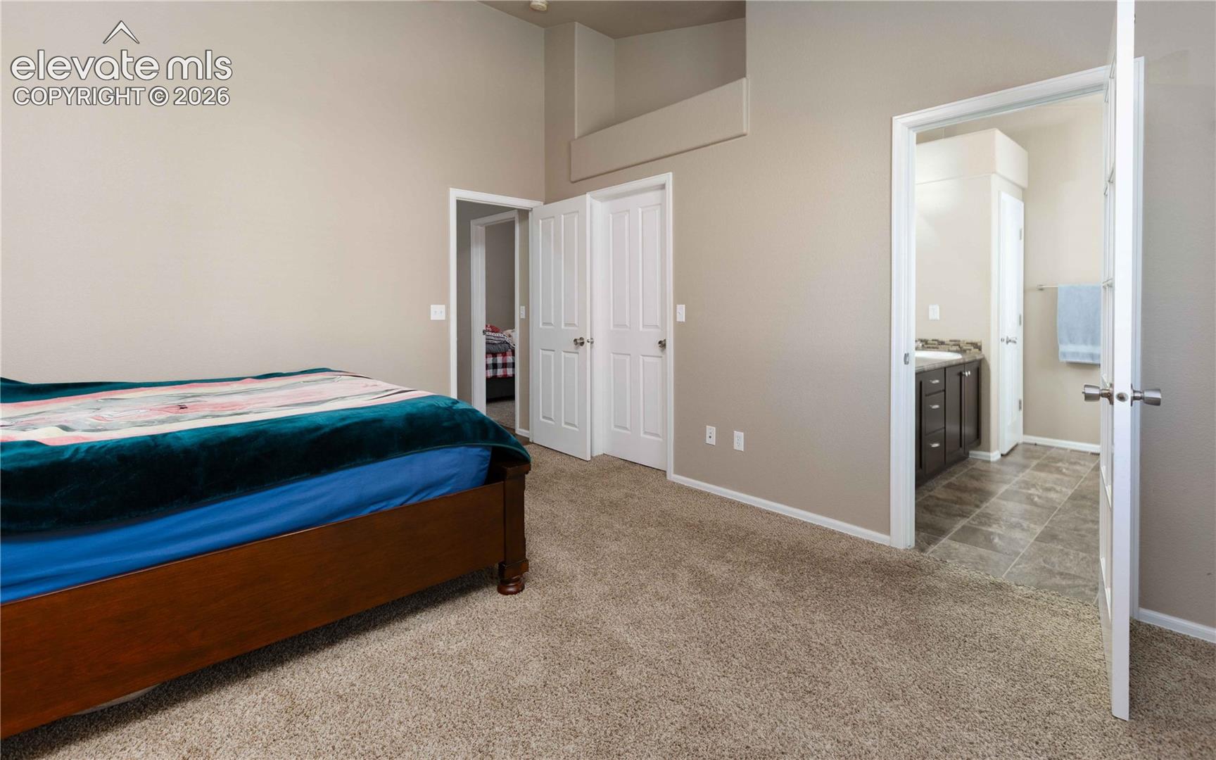 High-ceiling bedroom featuring neutral-tone walls, wall-to-wall carpeting, and double-panel doors