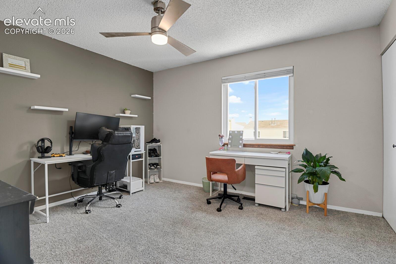 Wall-to-wall carpeting with a neutral finish, a ceiling fan with integrated lighting, multiple wall-mounted shelving units, and a window with blinds