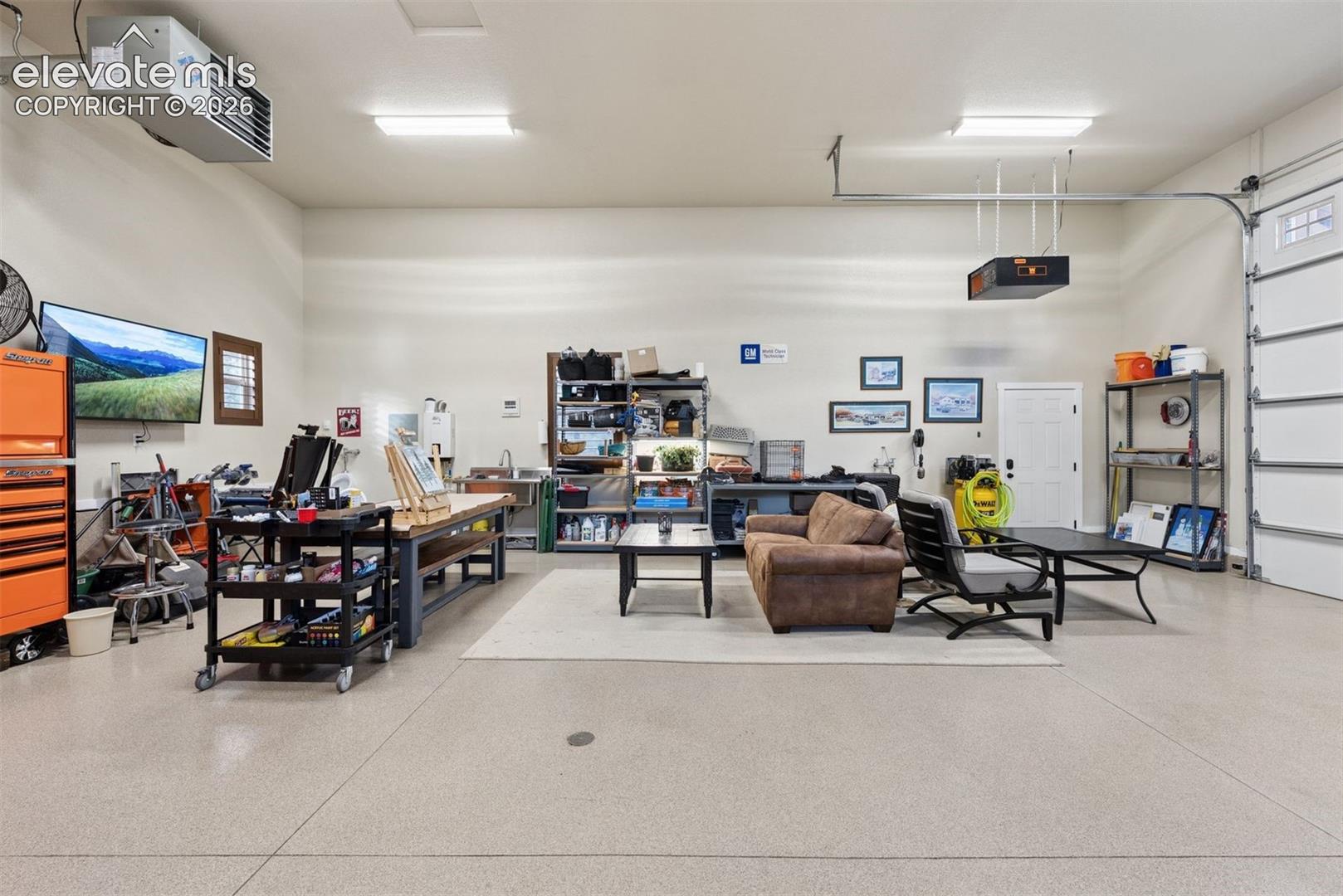 Spacious garage featuring an epoxy-coated floor, high-output ceiling-mounted heater, built-in utility sink, and LED overhead lighting