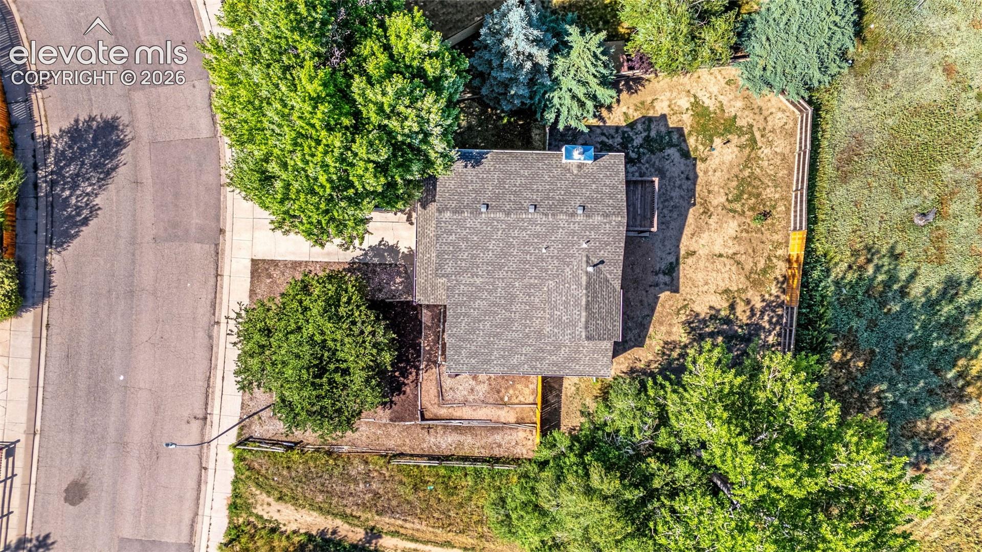 Aerial perspective of a property featuring mature trees, corner lot positioning, fenced perimeter, and a concrete driveway