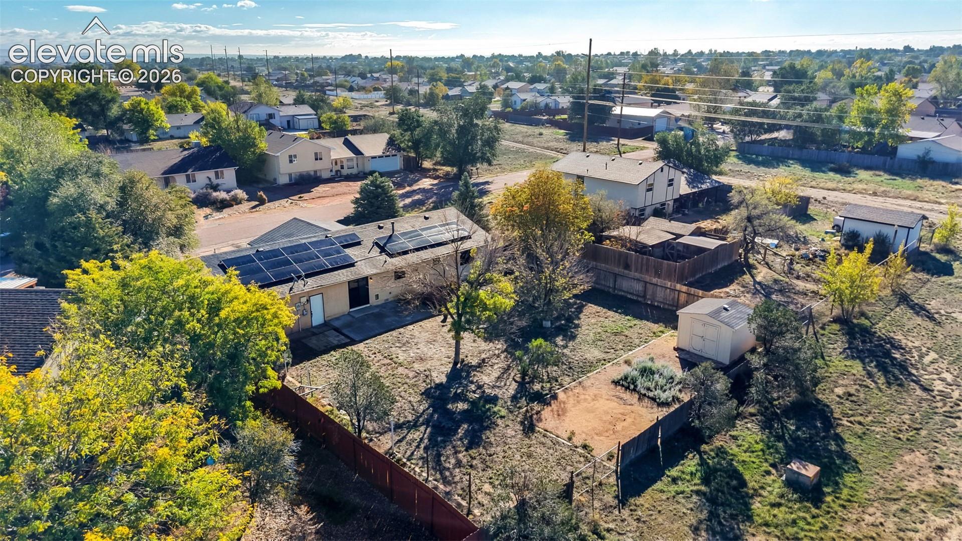 Aerial perspective of property featuring roof-mounted solar panels, a fenced backyard, and an outdoor storage structure