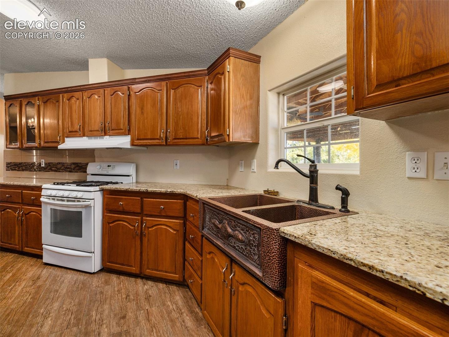 Kitchen featuring wood cabinetry, stone-finish countertops, an apron-front hammered copper double-basin sink, matte black gooseneck faucet, and wood-finish flooring