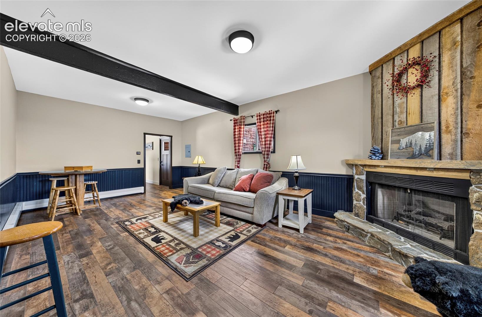 Wood-finish flooring, stone fireplace with a wood mantle, wood paneling, wood beam, and wainscoting