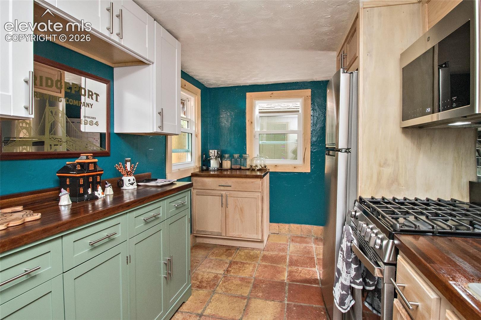 Kitchen featuring two-tone shaker-style cabinetry, wood-finish countertops, stainless steel appliances, and tile flooring