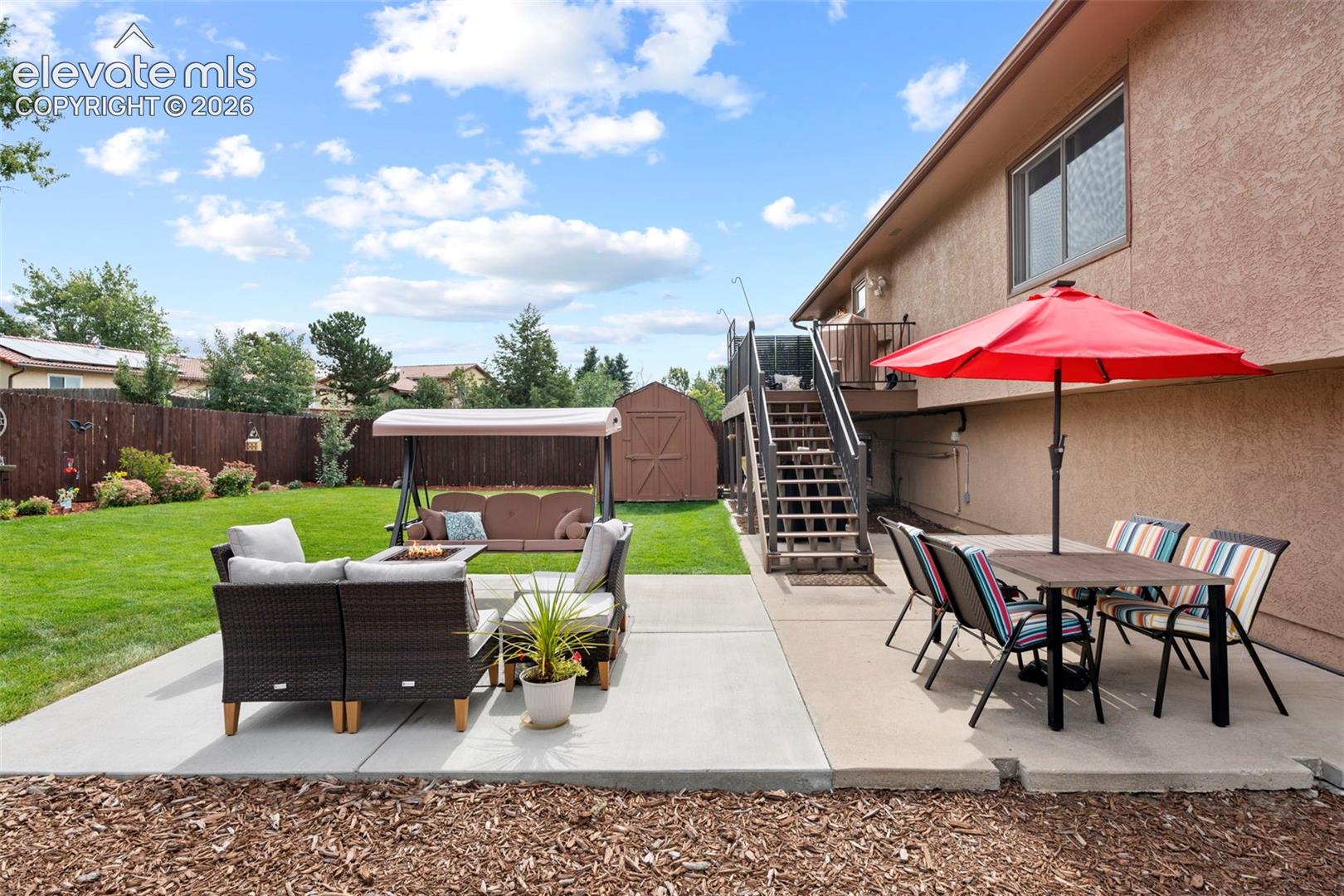 Fenced backyard featuring a manicured lawn, concrete patio, exterior staircase, and detached storage shed