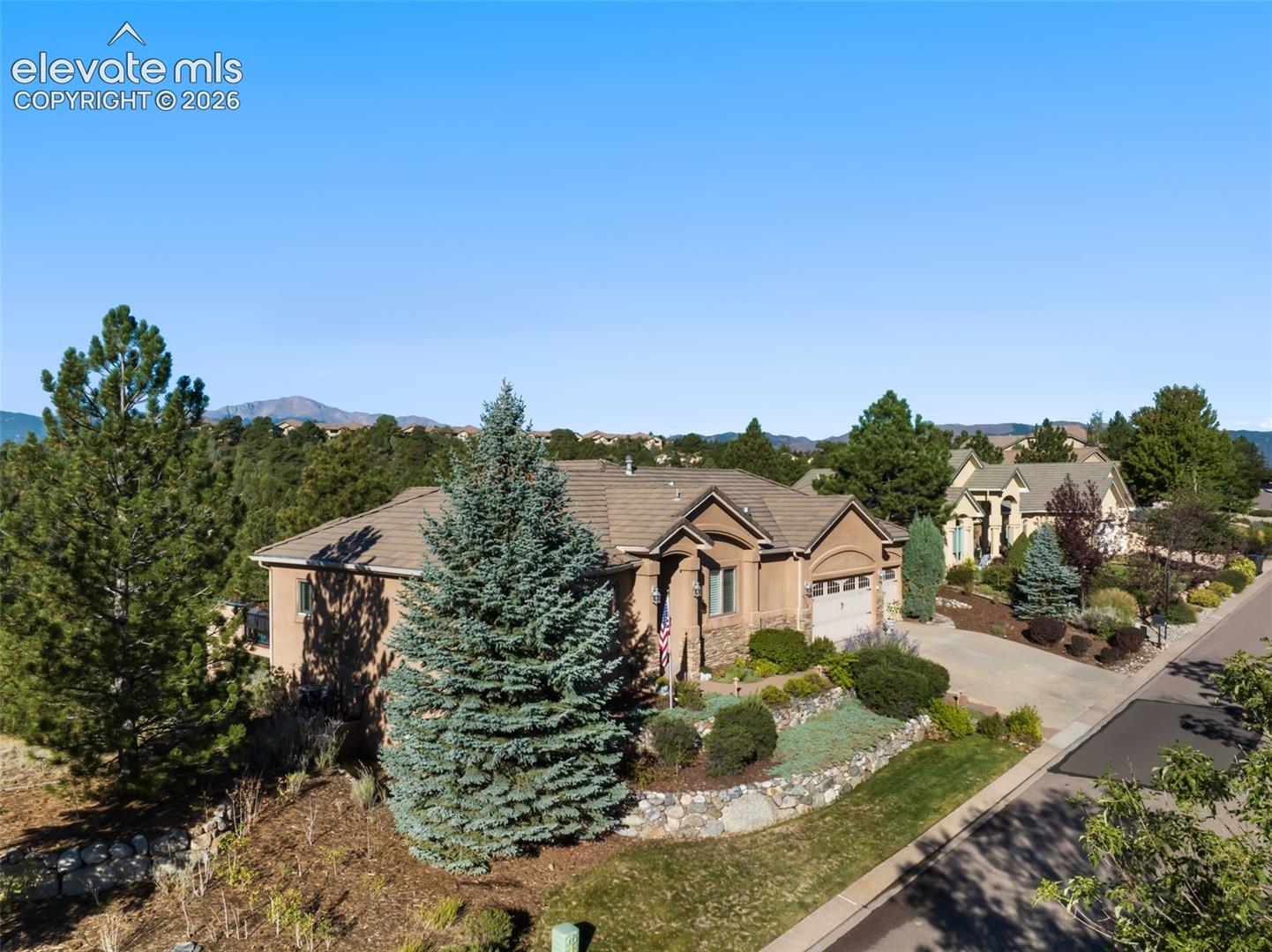 Single-story residence featuring a stone and stucco exterior, concrete driveway, attached garage, terraced stone retaining walls, and mature landscaping