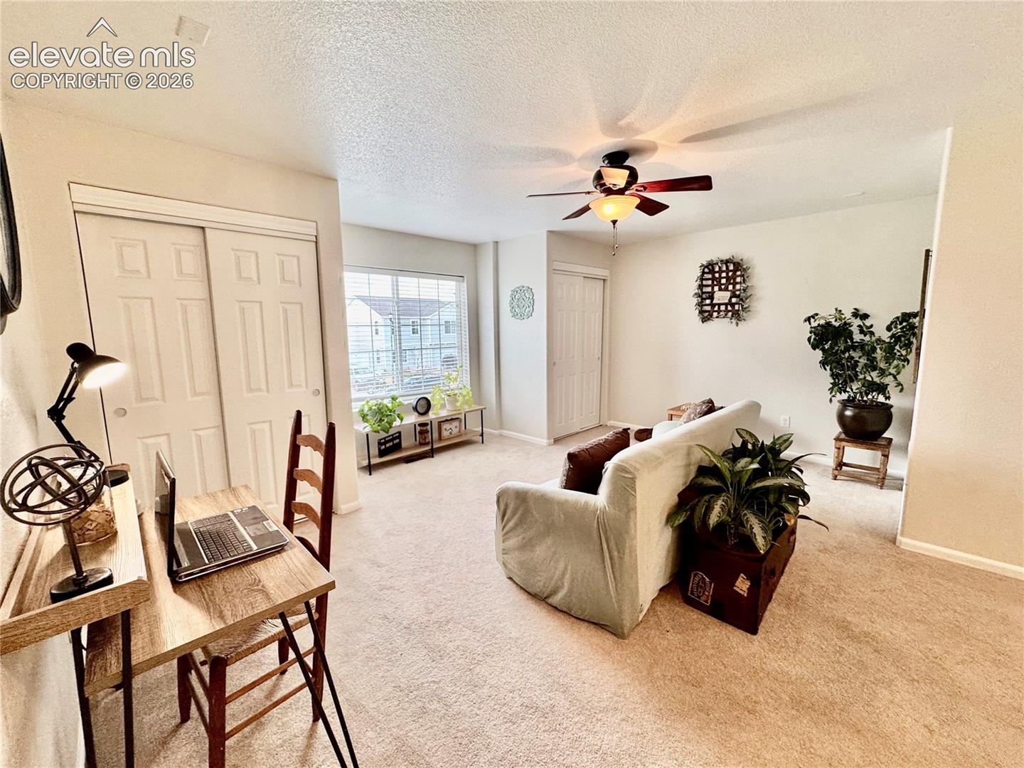 Carpeted interior space featuring a ceiling fan with integrated lighting, a large window with blinds, and a built-in closet with sliding panel doors